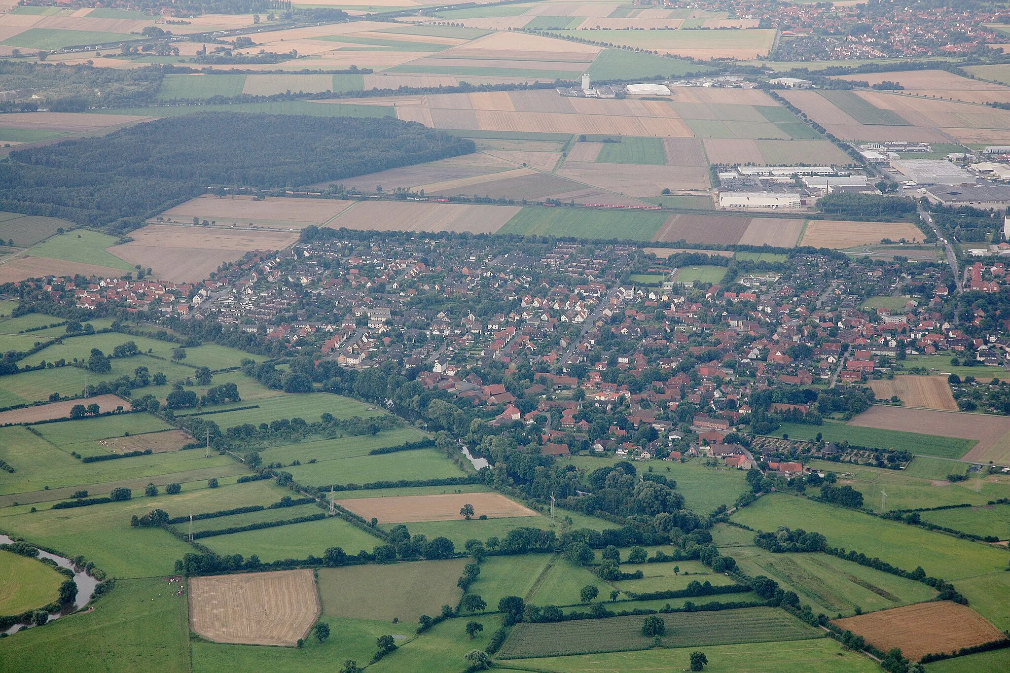 Photo showing: Aerial shot of Luthe, a suburb of the town of Wunstorf near Hannover in Germany. The river Leine is visible in the bottom left, in the background the railwayline Hannover-Minden runs through the image with freight train and a red local commuter train visible.