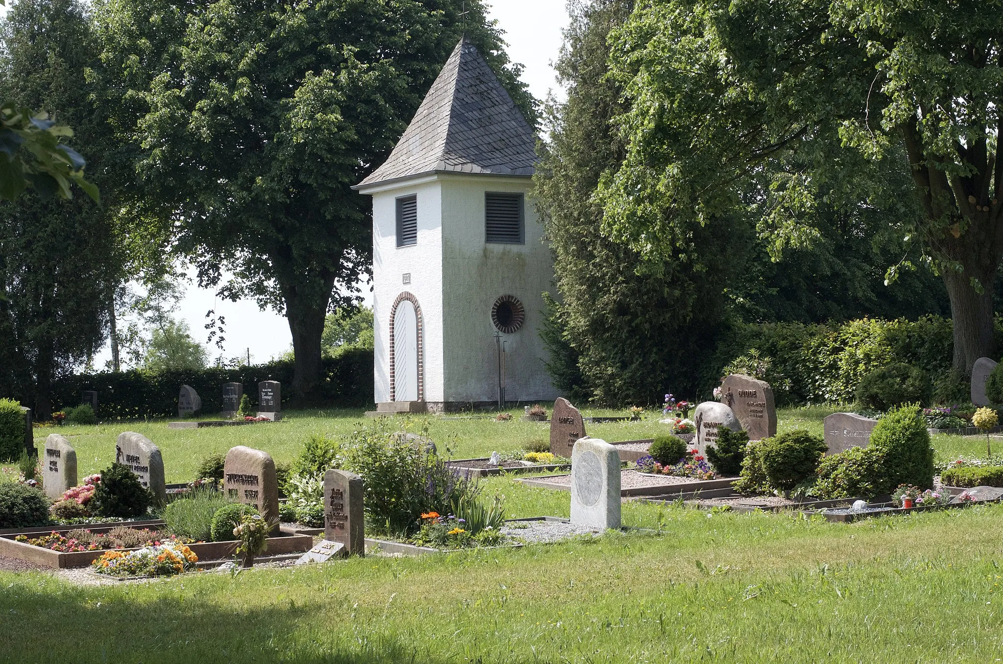 Photo showing: Blick über das Gräberfeld auf den Turm zu. Der Friedhof ist von einer Hecke gesäumt und hat zwei Eingänge zur Straße.