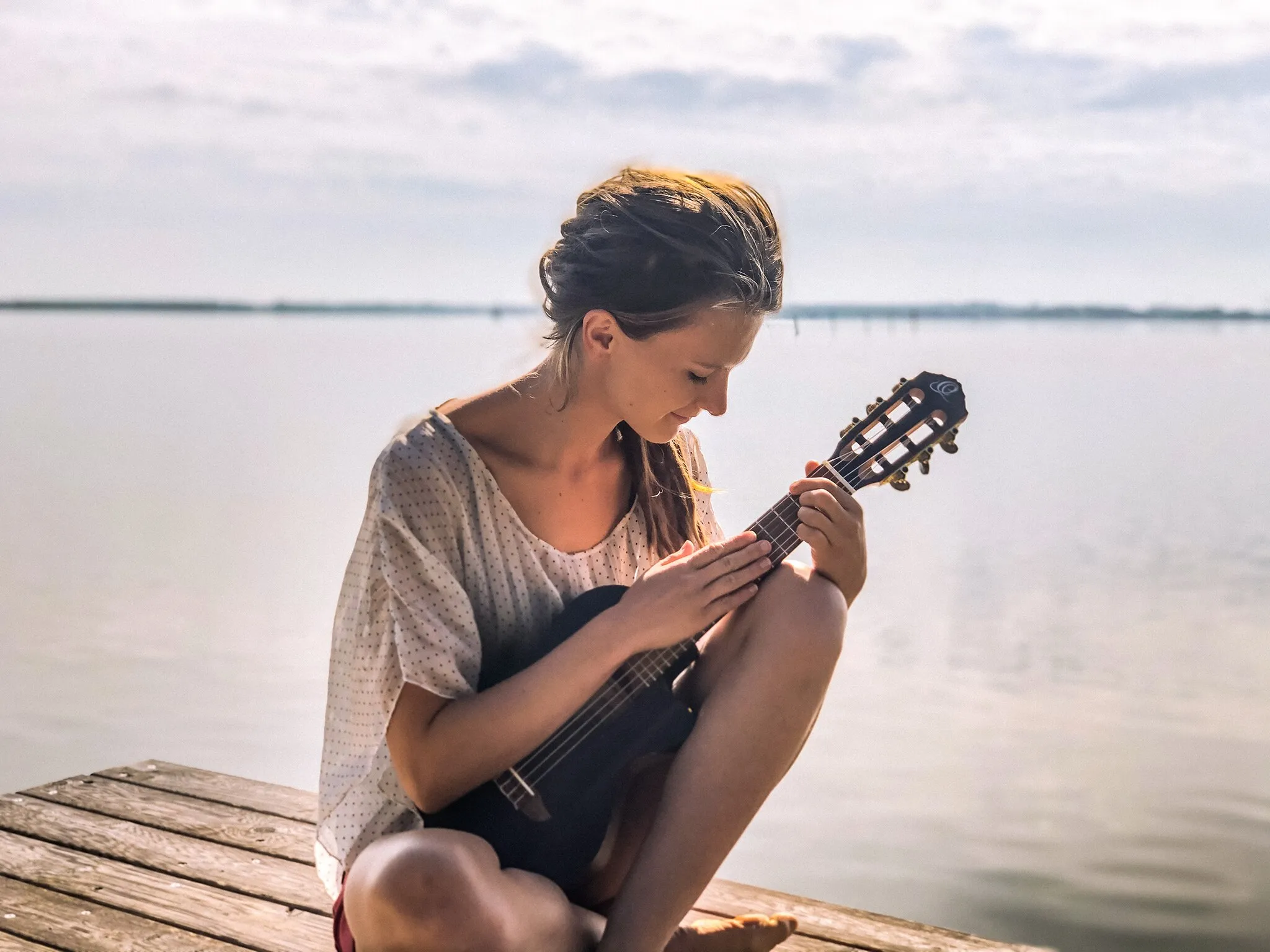 Photo showing: A picture of the artist Ronja Maltzahn, playing a guitalele by a lake.
