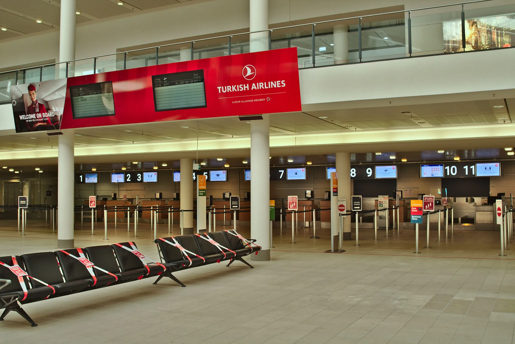 Photo showing: Departure hall of terminal 1 of Bremen Airport, deserted and with unmanned check-in counters during the Covid-19 crisis. Only one passenger aircraft per day departs here. On the bench in the foreground, every second seat is fenced off to comply with the applicable social distancing rules.