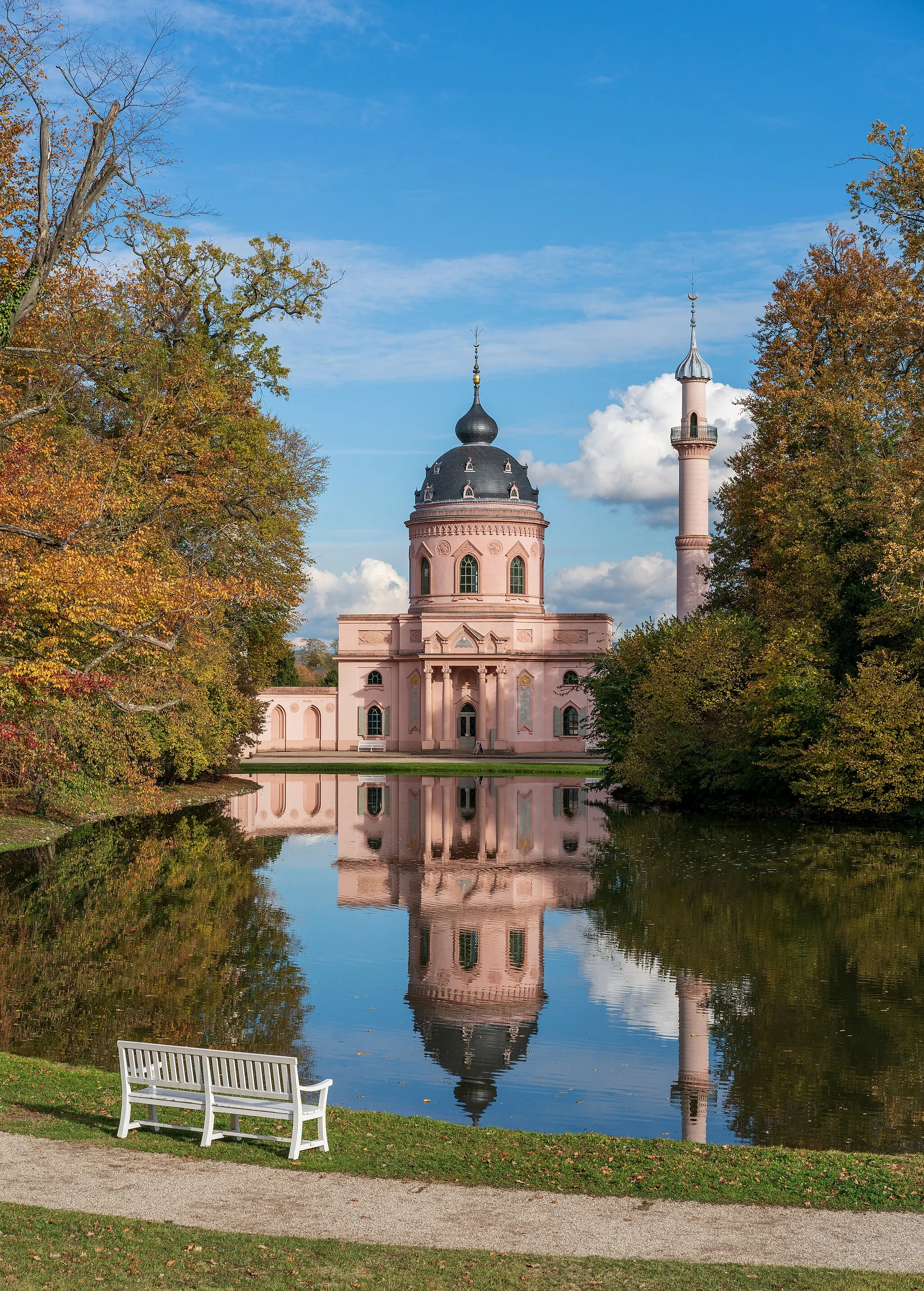Photo showing: Autumn view of the Red mosque in the gardens of Schwetzingen Palace, Germany. This listed building, constructed in 1779–1795 by Nicolas de Pigage as the first mosque-style building in Germany, was never a real Muslim mosque but was supposed to express the tolerance of the Enlightenment towards all religions. The photograph includes the so-called Moscheeweiher in front of the building, because the mosque was deliberately planned by de Pigage as a component of the park, and so I consider this as the view intended by de Pigage.
It was not possible to show the mosque completely from this point of view, as the trees always cover parts of it. But these trees are a part of the park ensemble, too, at least in its current state.