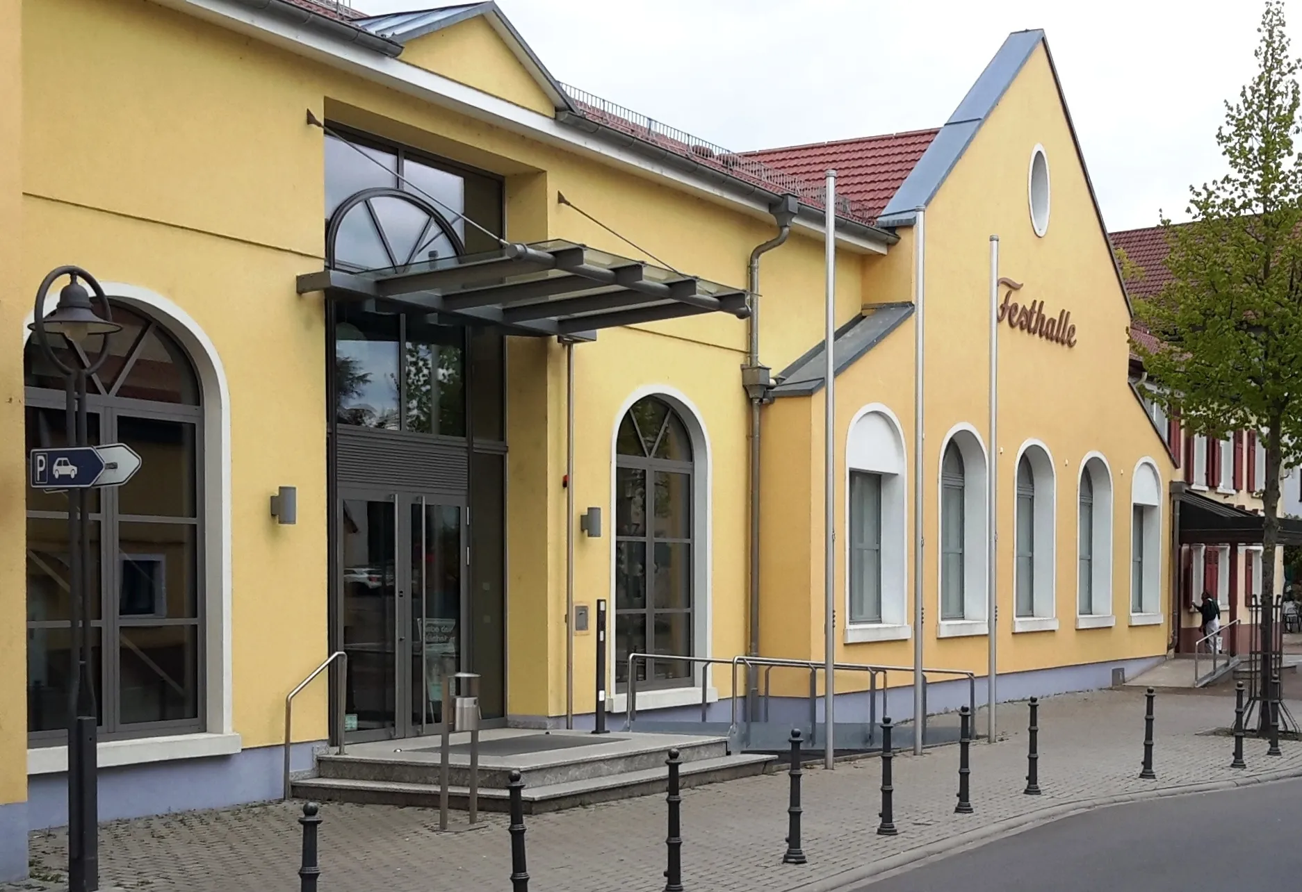 Photo showing: Bild der Festhalle, Hauptstraße 2 in D 68792 Brühl (Baden), von Südosten (Rathaus). Links der 2011 eingeweihte Foyer-Anbau, in der Mitte der 1962 eingeweihte Saalbau, rechts die 1734 als "Gasthaus zum Ochsen" eingeweihte jetzige "Ratsstube".