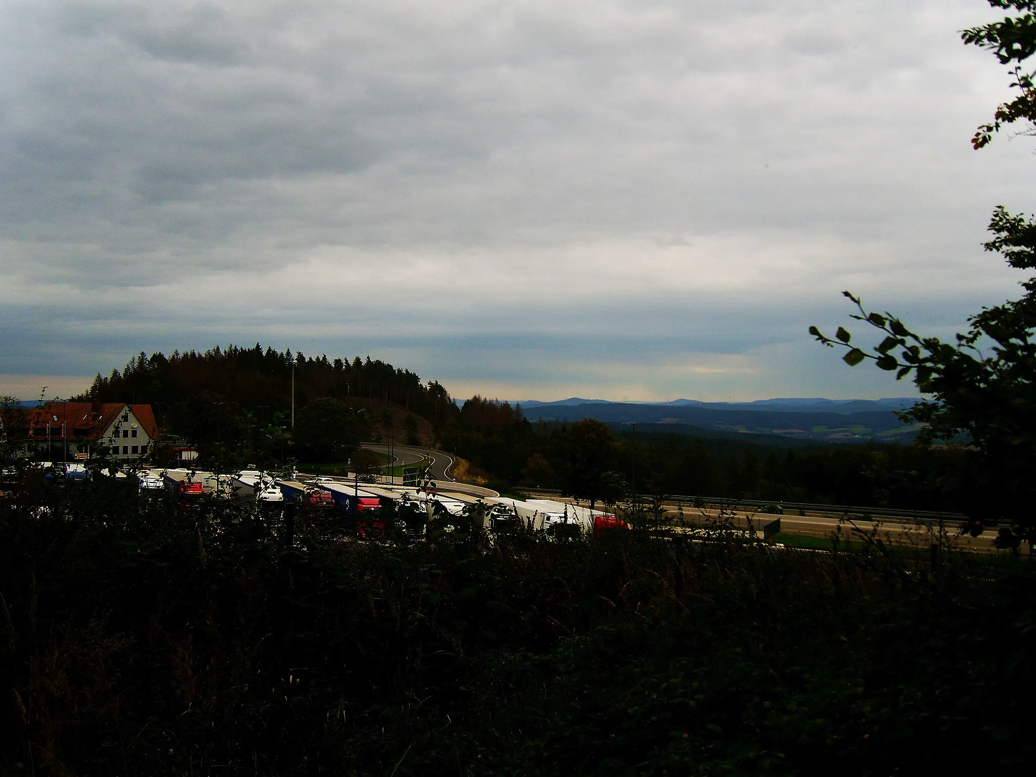 Photo showing: Blick von der Raststätte Rimberg in Richtung Rhön. Rechts des Rasthauses stechen insbesondere hervor:
Soisberg (630 m; 29 km)
Baier (714 m; 45 km)
Sachsenburg (721 m; 43 km) und Mannsberg (6990 m; 41 km); optisch miteinander verschmolzen
Roßberg (694 m) Der Soisberg geht nach rechts optisch fließend in den Dietrich (669 m; 39 km) über, links folgt ihm der optisch kleinere Öchsen (627 m; 39 km); links dahinter der Thüringer Wald mit dem Seimberg (803 m; 69 km - der Inselsberg (916 m; 70 km) weiter links ist vom Großen Bartküppel im Vordergrund verdeckt, kann indes ebenfalls bei guter Sicht vom Rastplatz aus eingesehen werden.
Rechts vor dem Soisberg die Mengshäuser Kuppe (473 m; 13 km), die Windmühlen stehen jedoch eine Reihe weiter, jenseits der Haune. Zwischen Soisberg und Baier im Hintergrund der Thüringer Wald mit Schmalkalder Loibe (886 m; 78 km) und Donnershauk (894 m; 82 km). Zwischen Baier und Sachsenburg sieht man nur bei allerbester Sicht den Großen Beerberg (983 m; 91 km).
Zwischen Manns- und Roßberg der Stoppelsberg (524 m; 17 km) vor dem Hessischen Kegelspiel. Der Appelsberg (531 m; 26 km) lugt rechts nur knapp hinter dem Stoppelsberg hervor, rechts davon der Stallberg (553 m; 27 km). Links des Stoppelsbergs schließen sich nacheinander Rückersberg (525 m; 25 km), Kleinberg (522 m; 29 km) und Lichtberg (465 m; 24 km) an.

Vgl. Udeuschle!