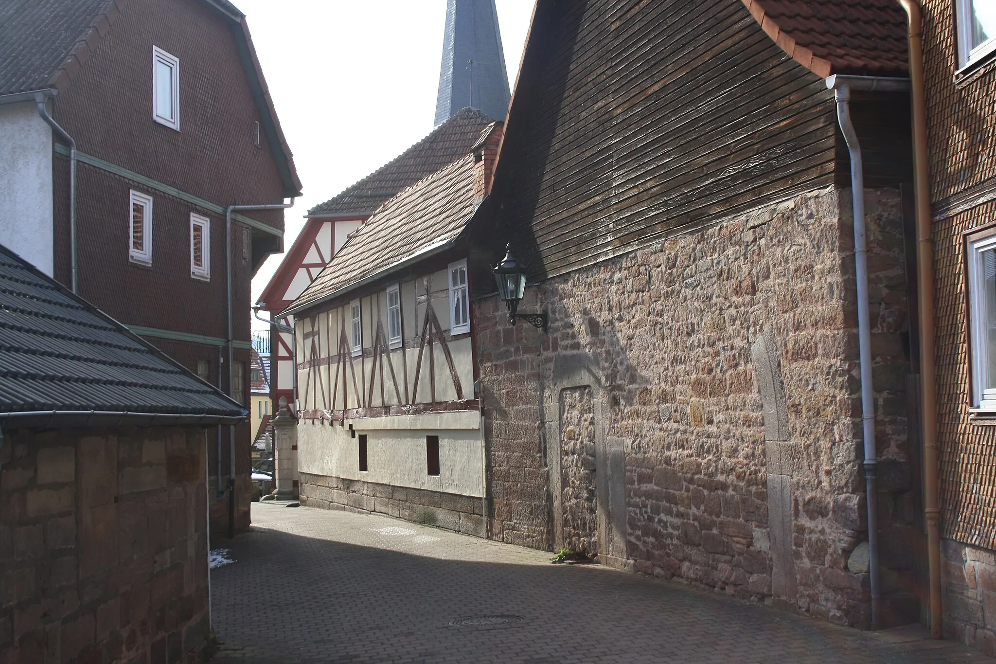 Photo showing: Sandsteinmauer mit erhaltenem Torbogen nahe dem Rathaus von Poppenhausen, im Hintergrund die Pfarrkirche