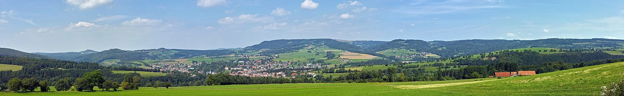 Photo showing: Gersfeld from (Rhön) from Rodenbach knoll (680 metres (2,230 ft)). Gersfeld is located at about 400 metres (1,300 ft) above sea level and is a recognized health resort and Kneipp spa town in the middle of the Hessian Rhön. At top center is the Wasserkuppe with radome, with an altitude of 950 metres (3,120 ft) the highest mountain in the Rhön. Top left of the 705-metre-high (2,313 ft) Wachtküppel. Right above the 926-metre-high (3,038 ft) Heidelstein.