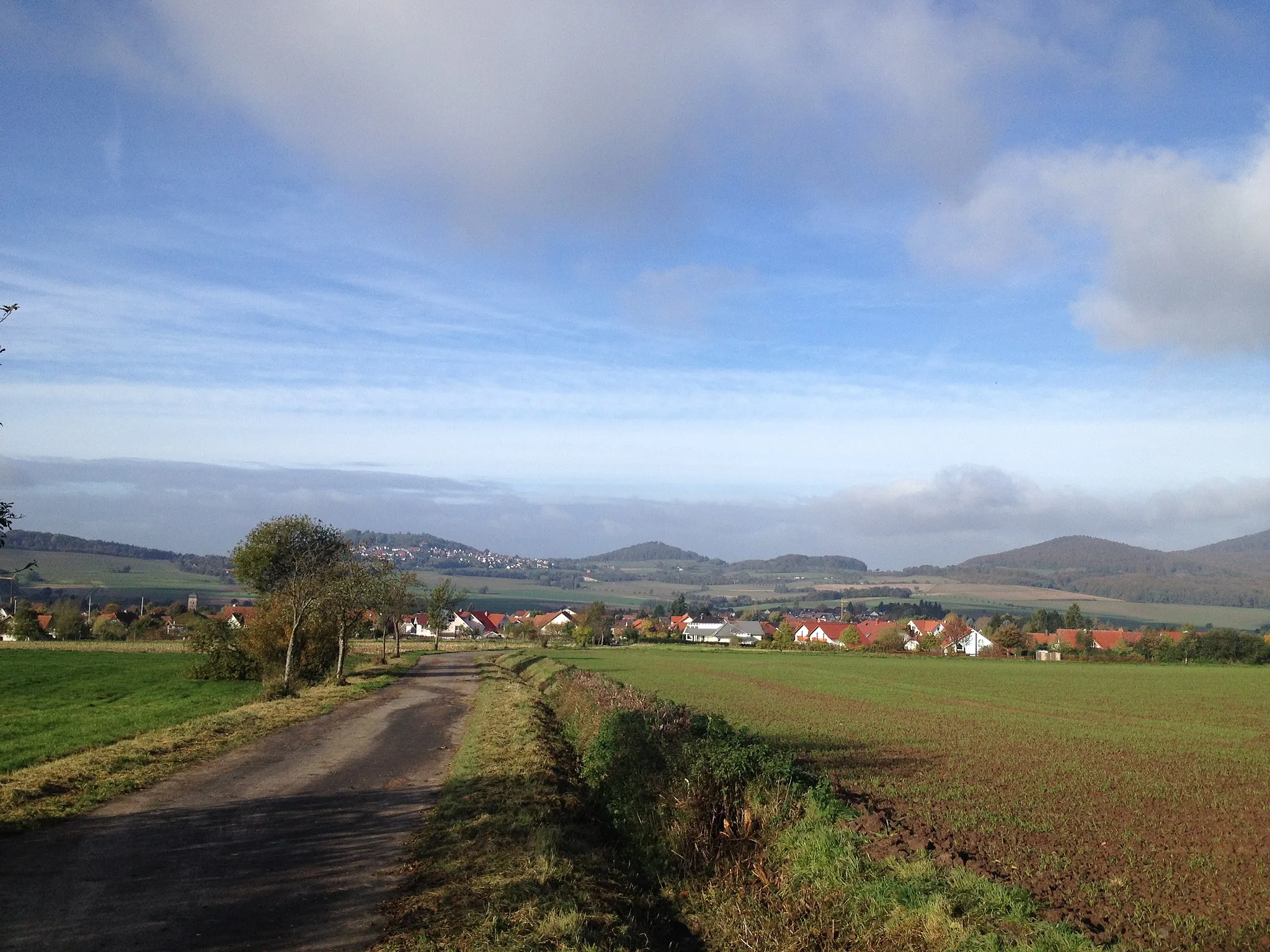 Photo showing: Blick von der Kohlenstraße östlich von Ehlen, über welche der Eco Pfad Kulturgeschichte Habichtswald und die lokalen Wanderwege ⊥ und E1 verlaufen, über Ehlen Richtung Burghasungen mit Hasunger Berg (links über Ort), Bosenberg (mitte) und Rohrberg (rechts)