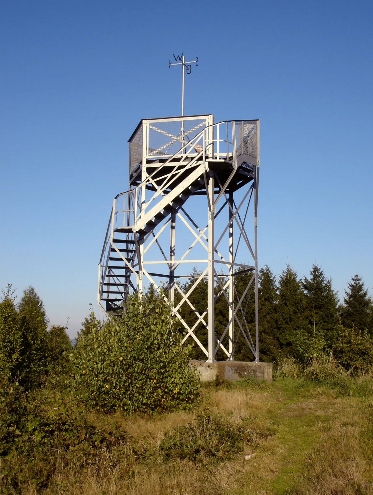 Photo showing: Peak of the mountain Gilberg (known as Gilbergskopf, 425.93 m ASL) with its observation tower in Siegen, Germany. The truss tower has a height of 5.56 m and was erected in 1888 on order by the Heimat- und Verschönerungsverein Eiserfeld. It is the oldest among the four observation towers in Siegen. View from the tower: See Image:Siegen Blick aus Sueden Sued-West.jpg.
