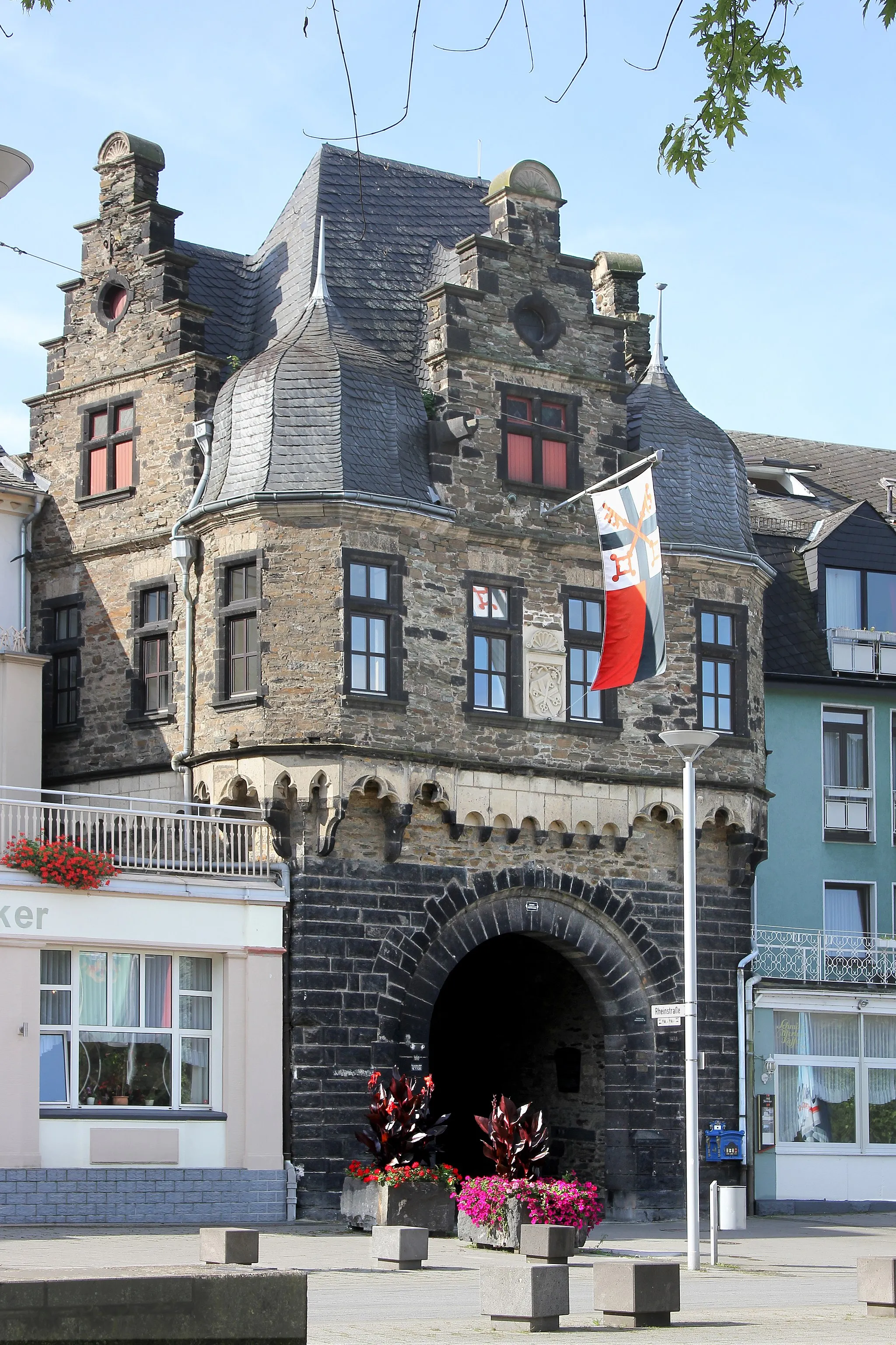 Photo showing: Andernach, Rheintor (Nordost), eine Doppeltoranlage, etwa aus der Zeit um 1200. Das Rheintor war eine der wichtigsten Anlagen der Stadtbefestigung. Im 15. Jahrhundert wurde das Außentor (Bild) umgebaut und erhielt einen neuen Oberbau auf Rundbogenfries und vorgekragte Ecktürmchen. Im 18. Jahrhundert wurde ein Mansarddach aufgesetzt. Im Innern der Toranlage stehen auf zwei Konsolen aus Tuff, Volksmund „Bäckerjungen“ genannt.