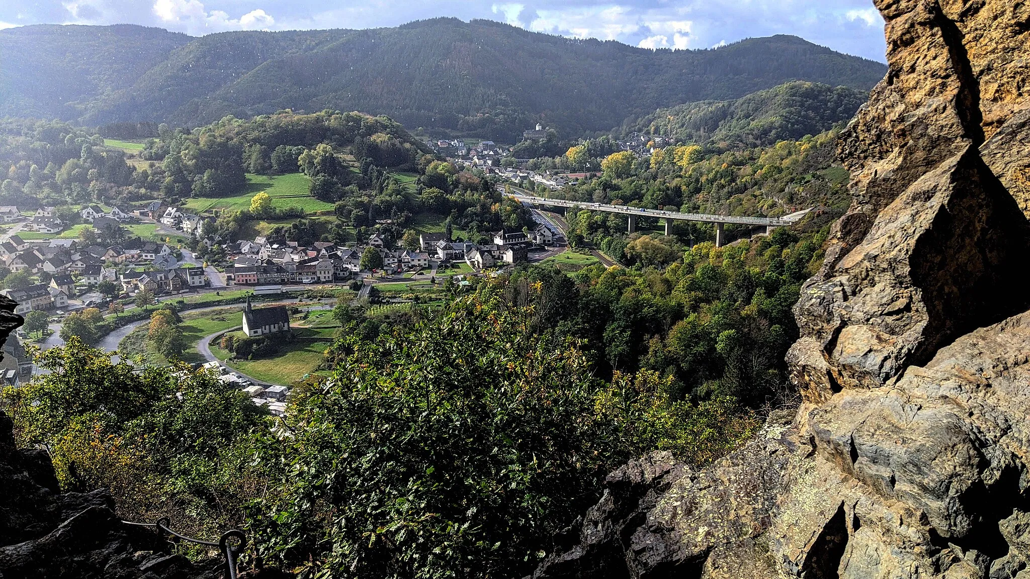 Photo showing: Blick vom Teufelsloch oberhalb von Altenahr auf die Ortsteile Altenburg und Kreuzberg, links unten die Maternus-Kapelle, im Hintergrund die Brücke der B257 und dahinter die Burg Kreuzberg