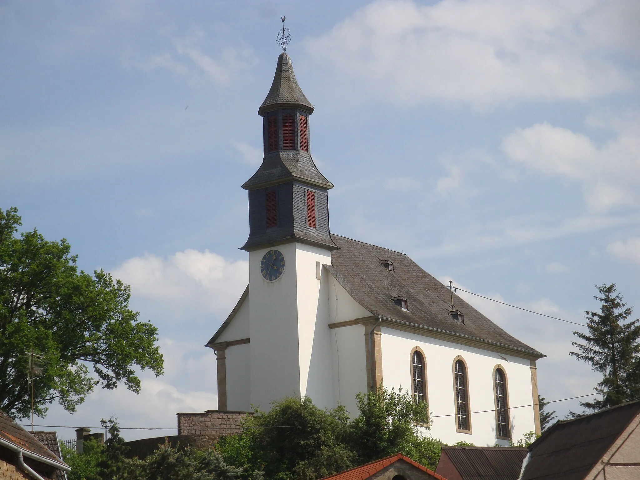 Photo showing: Die Kirche steht auf einer kleinen Anhöhe oberhalb des Ortes.
Hinter der Kirche befindet sich der Friedhof.