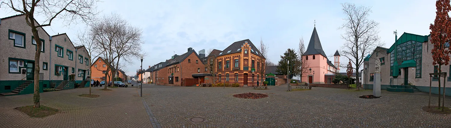 Photo showing: Köln-Rheinkassel Dorfplatz, Mitte St.-Amandus-Kirche, rechts und Links Teile der Amandus-Siedlung von Gottfried Böhm