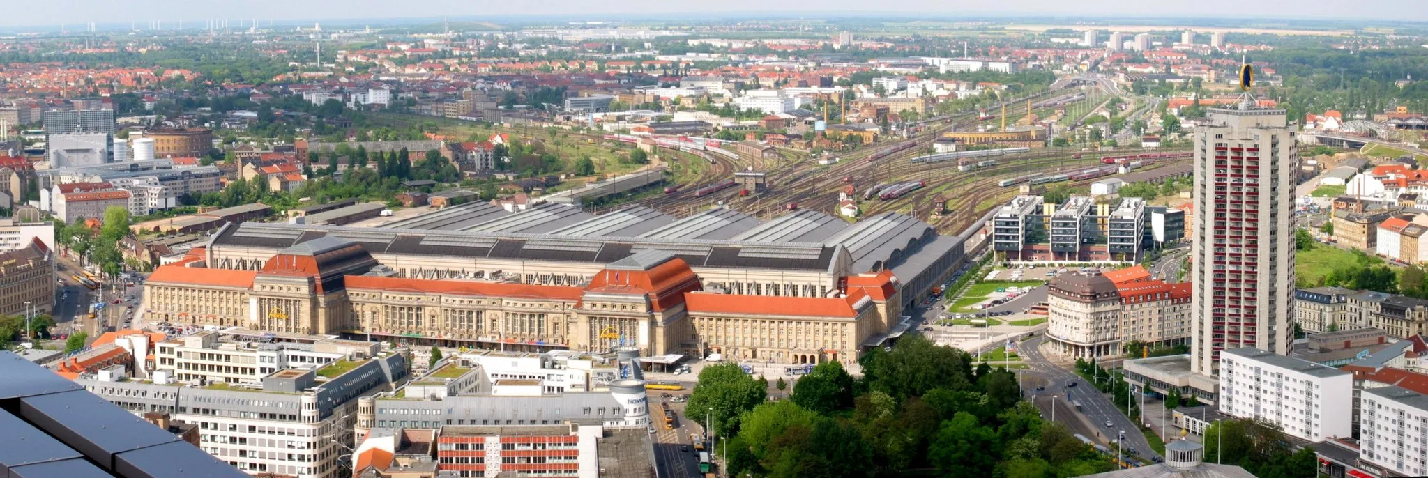 Photo showing: Leipzig central train station with its large track field
in front on the right a park with a pool (Schwanenteich), in front of the park the roof of the opera house (Oper)
on the right the high rise building Wintergartenhochhaus with the sign of Mustermesse (Leipzig fair), behind it the tracks to Engelsdorf – Riesa – Dresden (first German trunk line) and Stötteritz – Markkleeberg – Altenburg – Hof
the tracks to the north lead to Dessau – Bitterfeld and Torgau – Falkenberg/Elster
the line to the left leads to Halle and Plagwitz
on the left behind the station an old goods station (Freiladebahnhof), behind it the unused gas holder Gasometer Nord