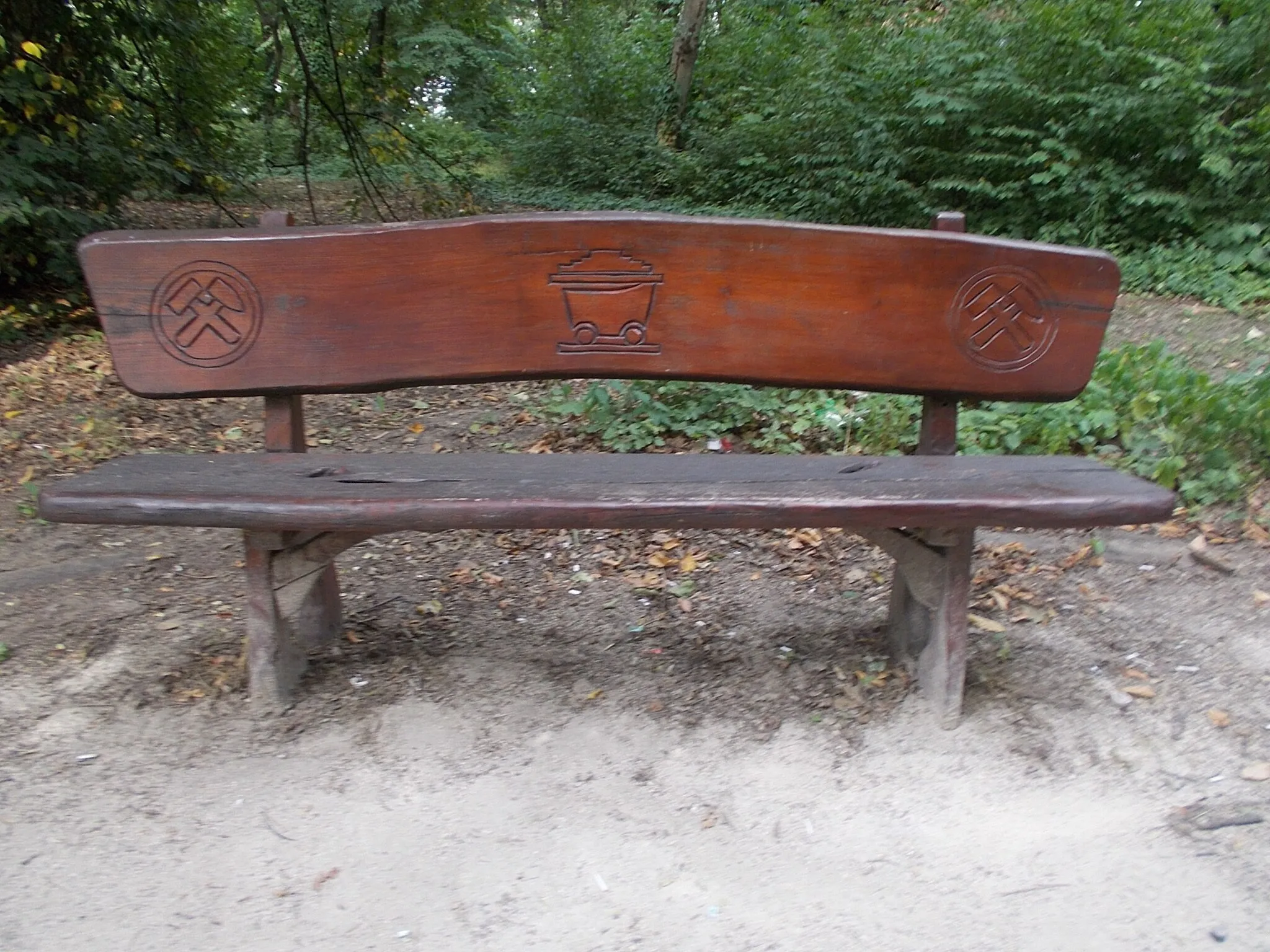 Photo showing: 'Mining cart' wooden bench /made in the local wood carving camp, c.2014-2015/. Next to its an information board about  "History of the Mining of Tatabánya  II 1901-1918" By about 1901, at the time of the construction of the railway station, the vertical transporters were already in operation, post office, telegraph, registry office comleted. By 1910 the eighth mine plant was completed, the steam-powered brick factory, and a briquette factory too. The Tatabánya  Sport Club, the mine rescue station was established. In 1912 a cement factory started to operate, the hospital was built, the old town church was built. In 1912 the MÁK Mining Co. was among the 50 largest companies in Europe partly due to the production of the Tata/Tatabánya coal basin. In 1914, the so-called railway coal pillar mining was started.  1915, due to the flood of the Galla-patk, the production of the Mine of Géza Teleki, No. 3, was stopped. 1917-1918 was a time of strikes. - About 'Mining cart' memorial bench information board: this is a four-wheeled small railway carriage in which the material produced in the mine is brought to the open air on narrow-track railways Towed by hand, with the help of a horse, with an infinity rope or locomotive. Cargo weight: 500-1400kg - Május 1. park, Óváros neighborhood, Tatabánya, Komárom-Esztergom County, Hungary.