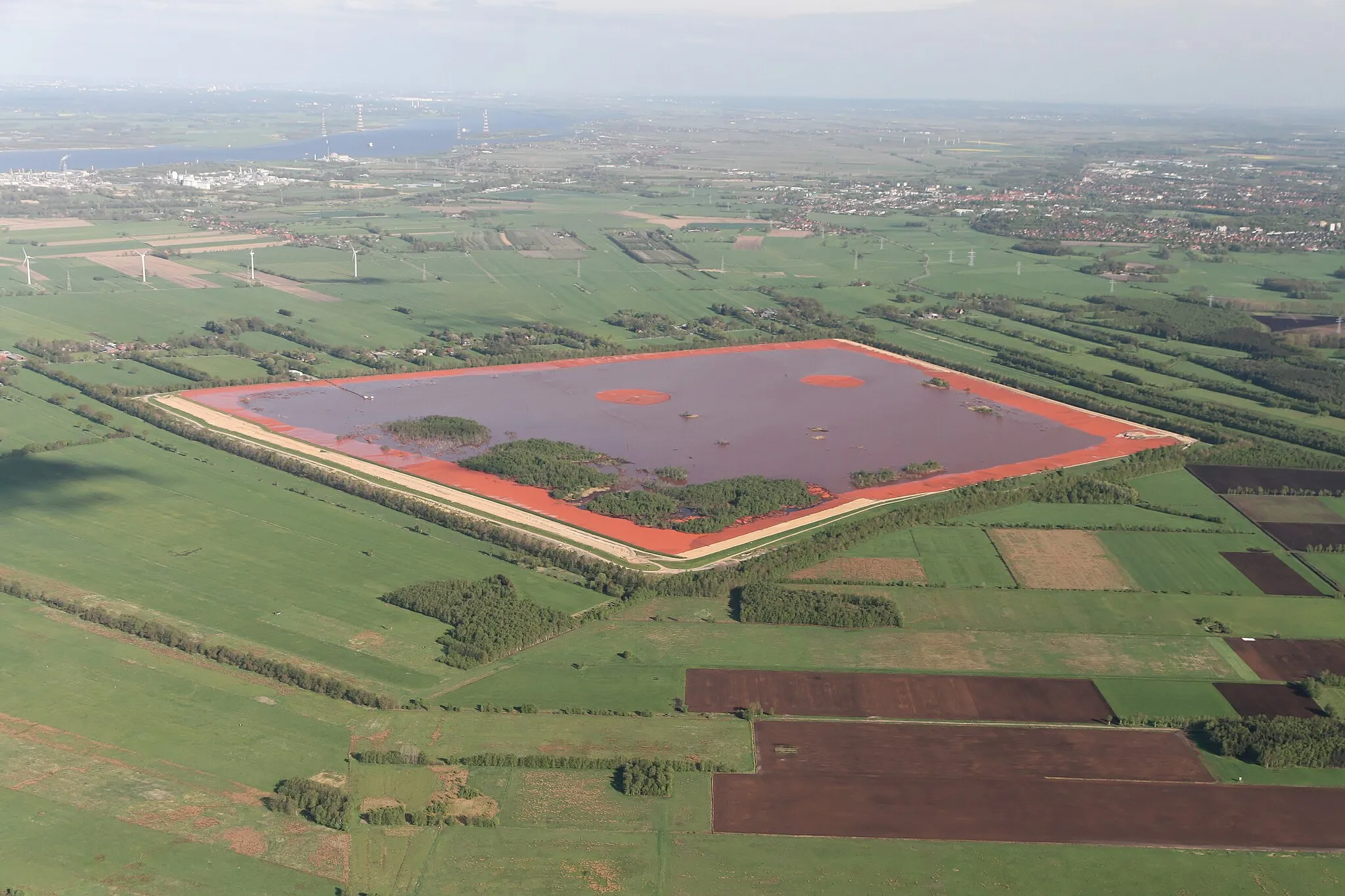 Photo showing: Blick von Westen op de Roodslammdeponie, Bützfletermoor an de Achterkant von de Deponie, ganz in'n Achtergrund de Elv mit Bützfleet, dat Industrierebeed Bützfleet (links) un Stood (rechts).