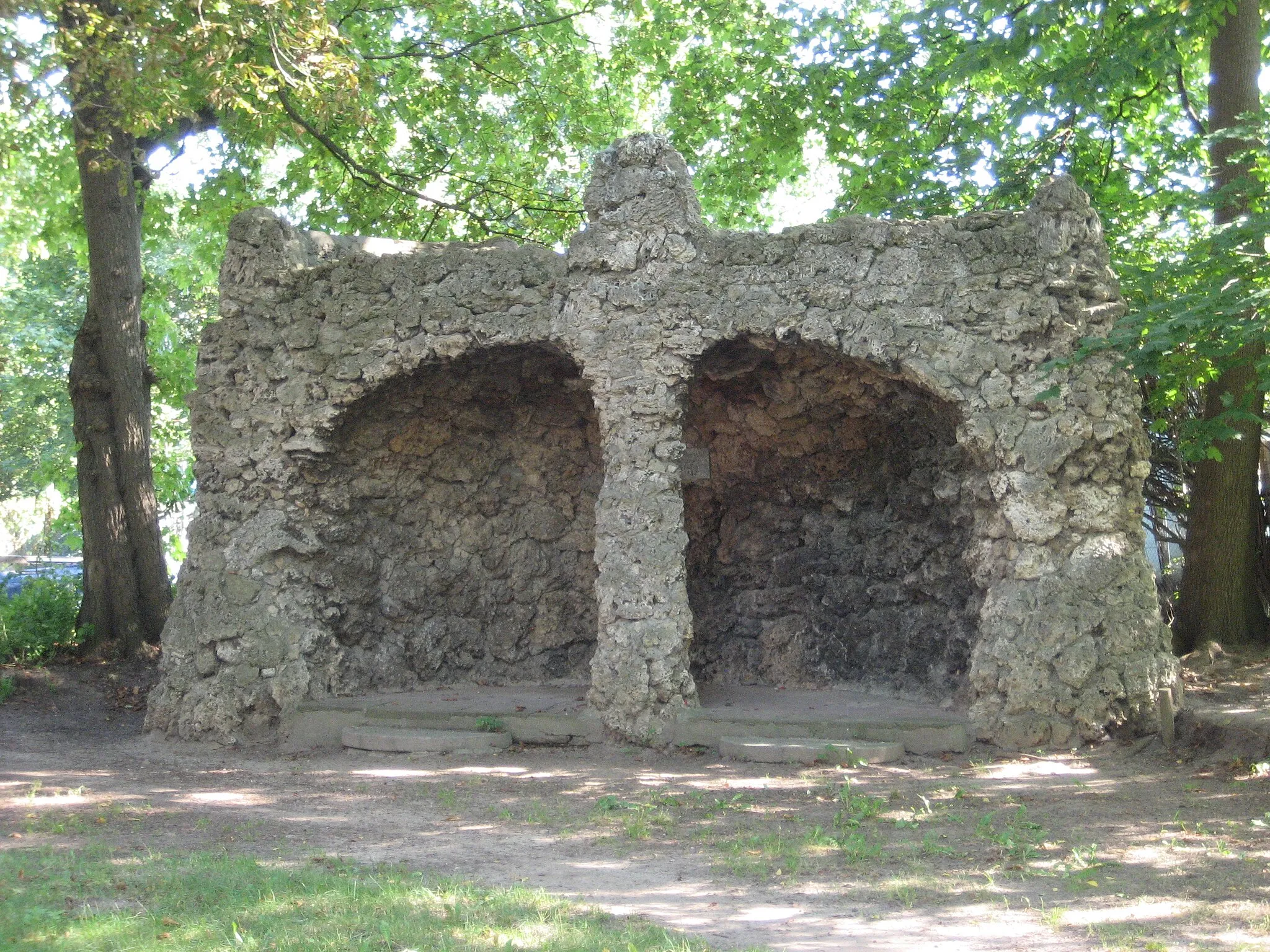 Photo showing: Der Bürgerpark entstand 1898 auf Initiative des Pasewalker Bürgermeisters Albert Will. Im Jahr 1903 wurde ihm zu Ehren die Liebesgrotte errichtet, eine aus Tuffstein erbaute Höhlenformation, in deren Innern sich eine Gedenktafel befindet und die von der Rückseite aus mit einer Treppe begehbar ist. Von dort oben eröffnet sich ein Blick über den Park mit dem nur wenig entfernt liegenden Goldfischteich.