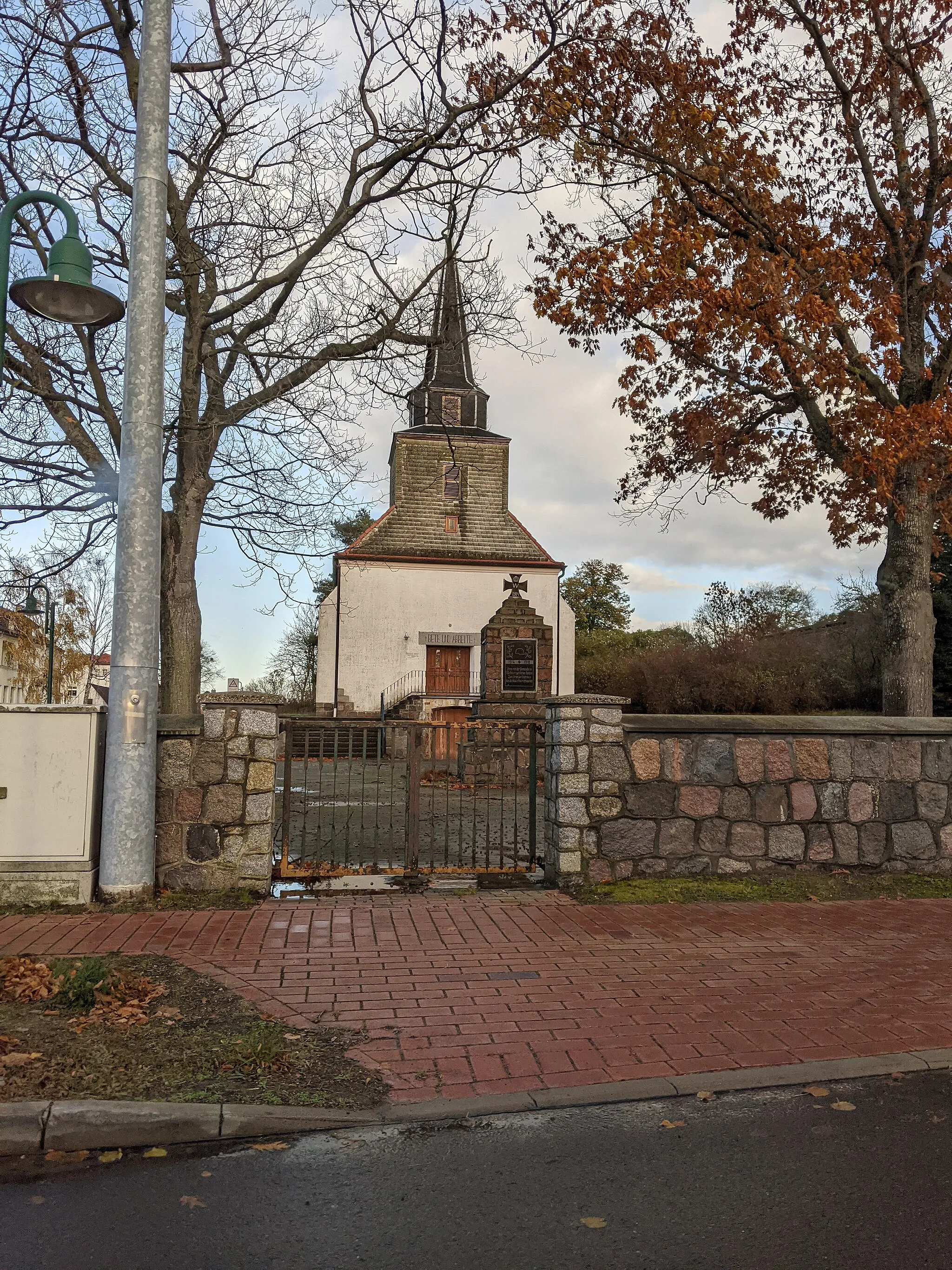 Photo showing: Dorfkirche in Heinrichswalde von der Dorfstraße aus gesehen. Vor der Kirche befindet sich ein Kriegerdenkmal.