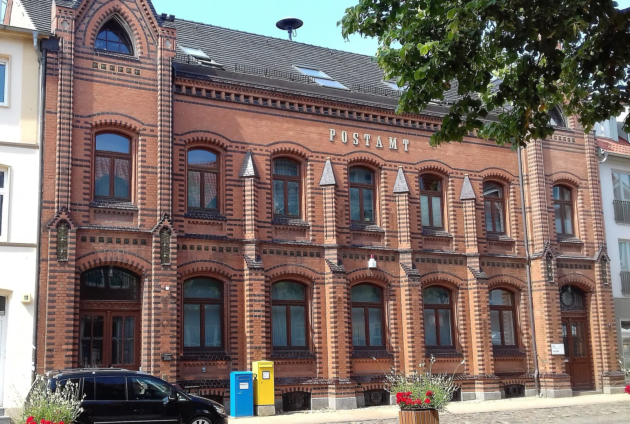 Photo showing: Das zweigeschössige Backsteingebäude aus roten Klinkern wurde von 1882 bis 1886 als "Kaiserliches Postamt" im Stil der Postgotik erbaut. Die Straßenfront wird durch glasierte Ziegel geprägt, die beiden Eingangsbereiche weisen Dreiecksgiebel auf, welche mit Risaliten bekrönt sind. 1969 erfolgten die Modernisierung der Schalterhalle und der Einbau der Fenster. 1994/96 wurden das Dach und die Fassade saniert sowie 1998 die Schalterhalle nochmals umgestaltet.