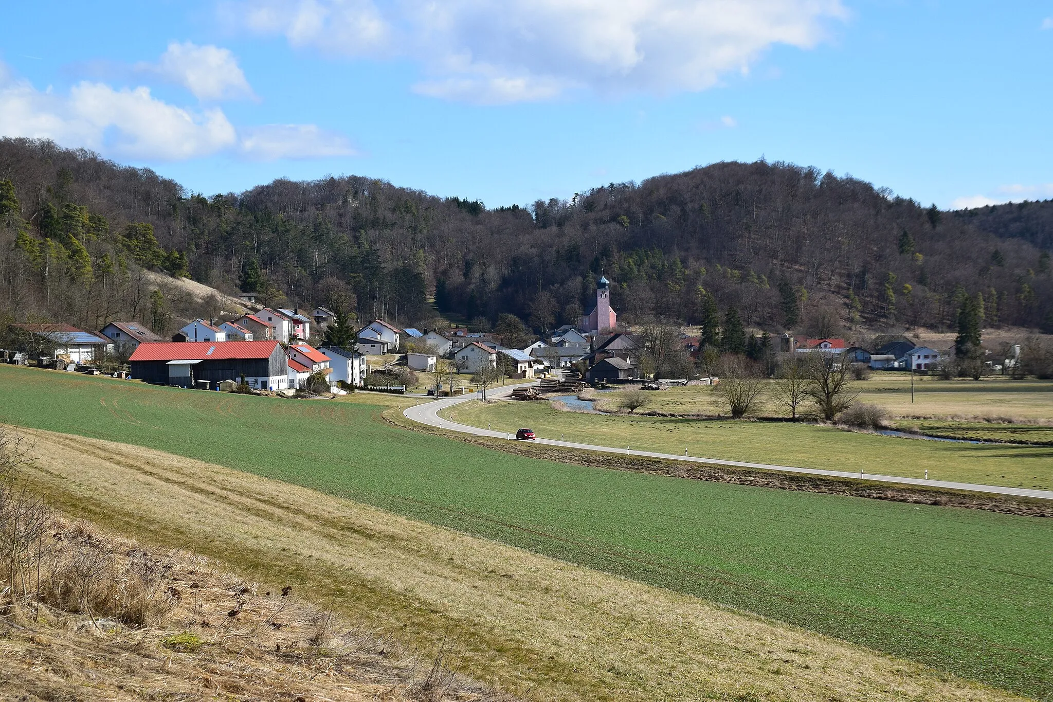 Photo showing: Dorf, Kirche, bewaldete Hügel, Feld, Straße