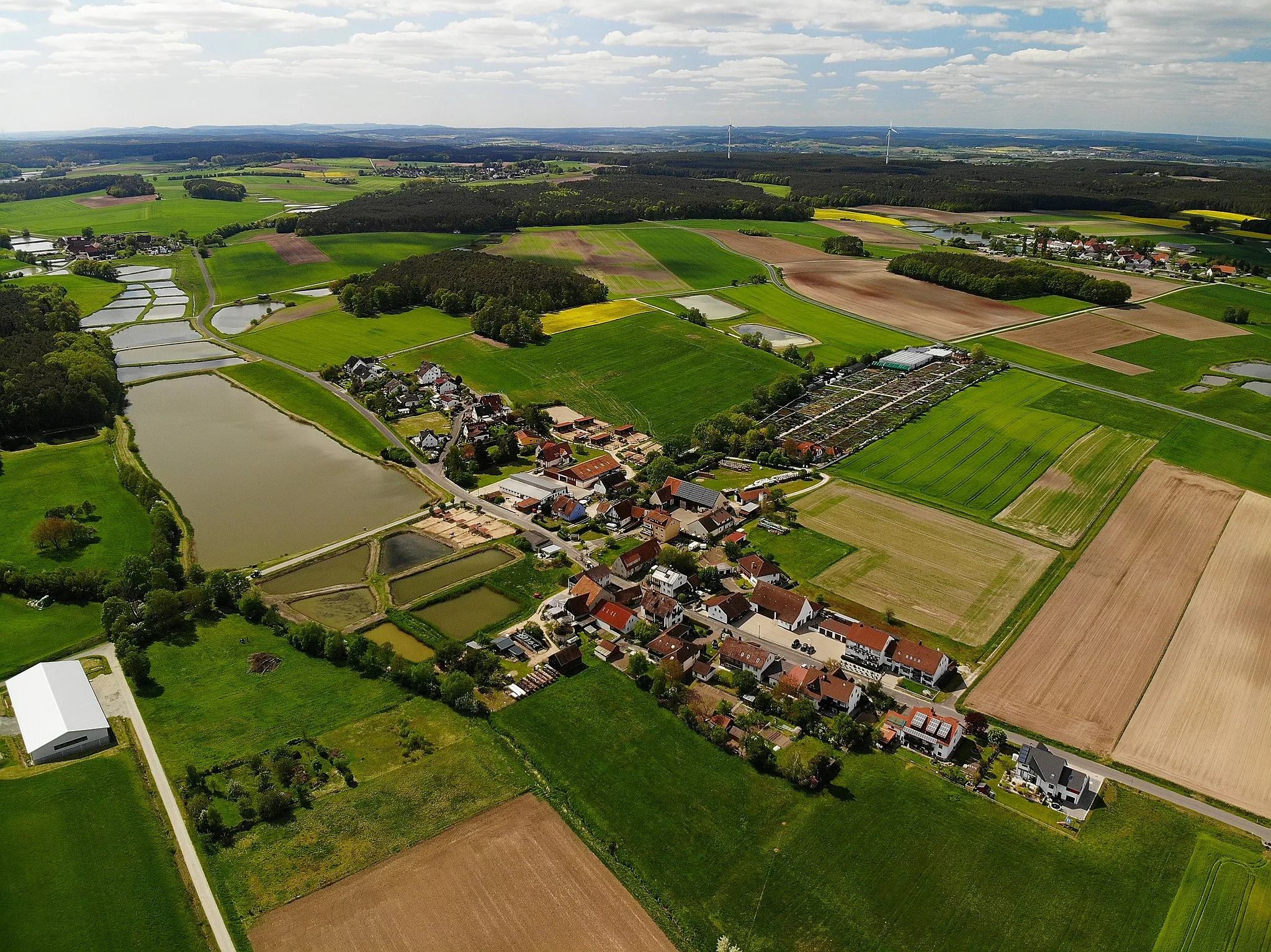 Photo showing: Aerial photograph of Mitteldorf, a district of Weisendorf, a town in northern Bavaria. In the background, additional districts of Weisendorf can be seen:
Sintmann, in the left background
Rezelsdorf, in the center background
Sauerheim, in the right background