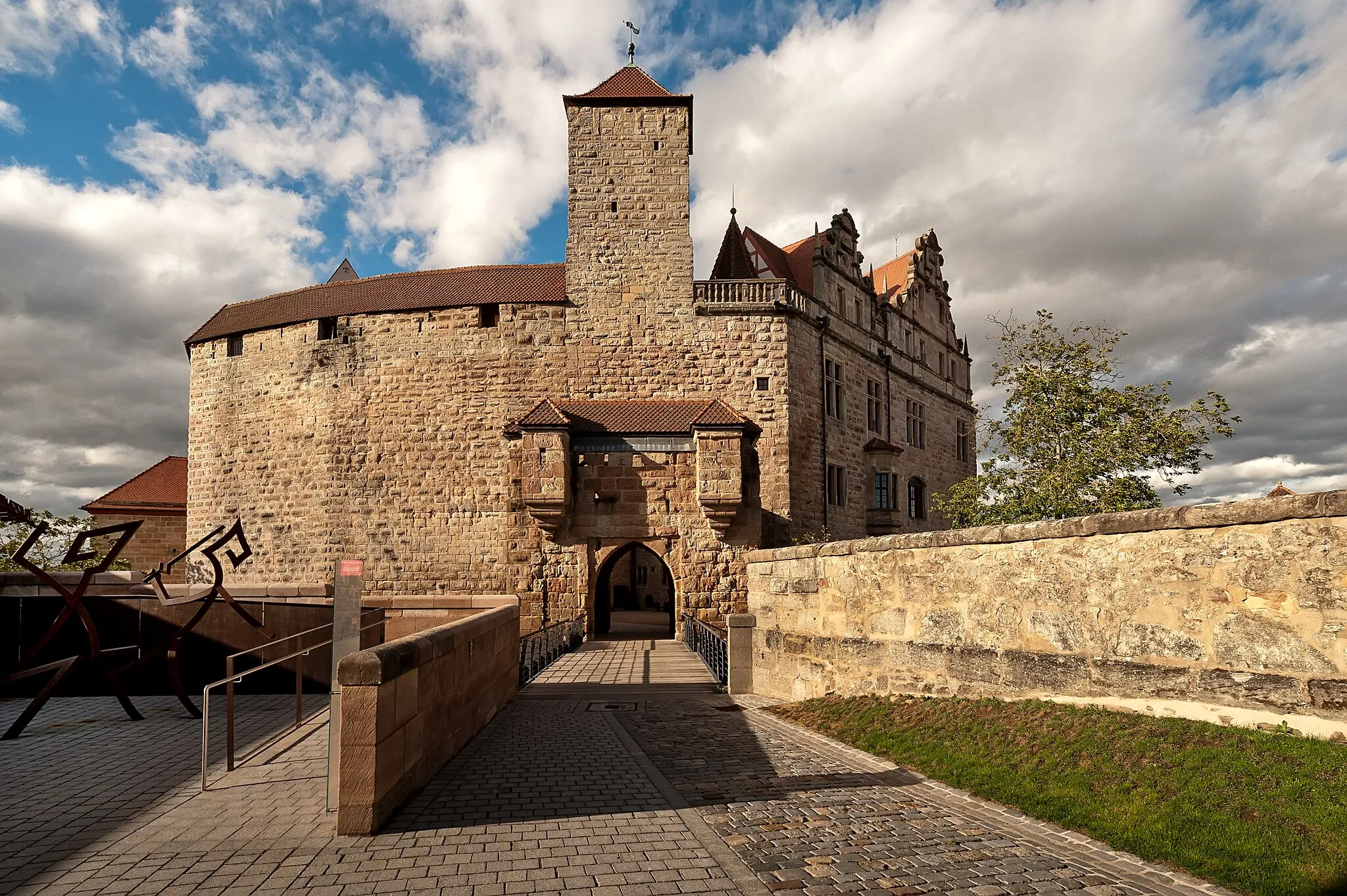 Photo showing: Hauptburg mit Sicht vom Schloßgarten von Hohenzollern - Langgestreckte unregelmäßige Burganlage in Spornlage mit Altem Bau, viergeschossiger Sandsteinquaderbau mit steilem Satteldach und angebautem quadratischem Folterturm, oberstes Geschoss traufseitig Fachwerk, Neuem Bau, dreigeschossiger zweiflügeliger Sandsteinquaderbau mit Satteldach, polygonalem Treppenturm mit Zeltdach und Renaissance-Sandsteingiebeln, Küchenbau, zweigeschossiger Sandsteinquaderbau mit Pultdach und großem Rauchabzug der sogenannten Ochsenbraterei, Kapellenflügel, dreigeschossiger Sandsteinquaderbau mit Satteldach und Dachreiter, Wehrgangshof mit nördlicher Ringmauer aus Sandsteinquadern und überdachtem Wehrgang, südliche Ringmauer mit überdachtem Wehrgang und Torturm gegen die Vorburg, Sandsteinquadermauerwerk, quadratischer Turm mit Zeltdach, Burganlage des 13.–15. Jahrhunderts, Neugestaltung 16. Jahrhundert, nach weitgehender Kriegszerstörung 1945 wiederaufgebaut