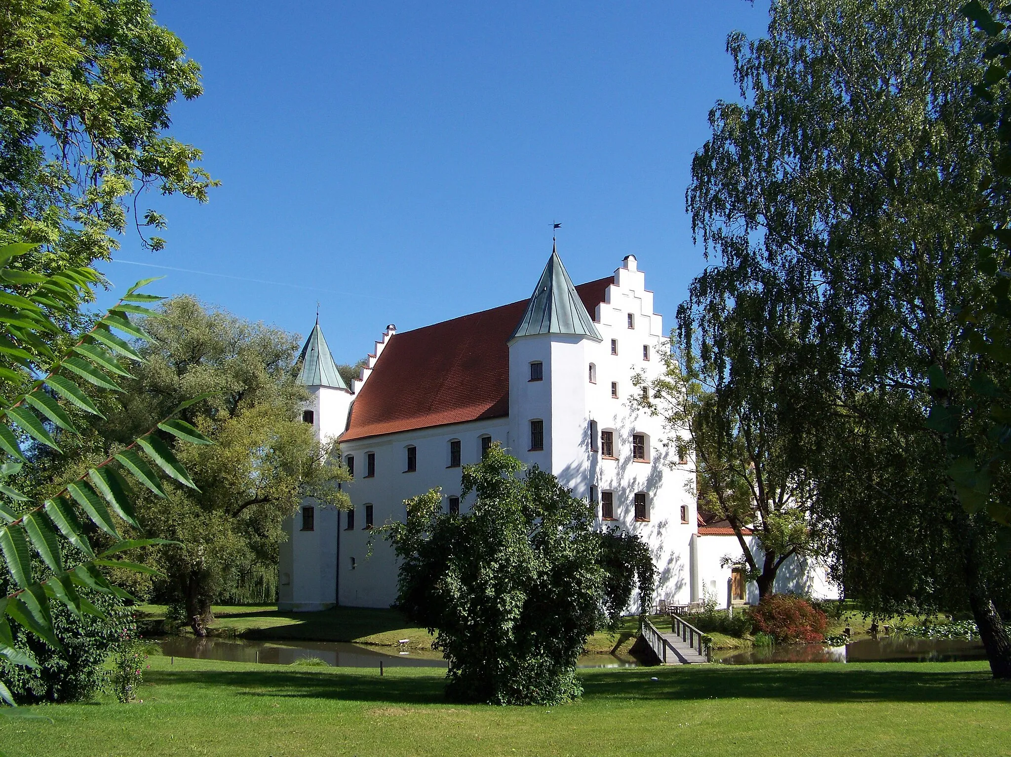 Photo showing: Straßkirchen, Schambach, Amselfinger Straße 4. Schloss, stattliche Zweiflügel-Anlage des 16. Jahrhundert, im Kern 12./13. Jahrhundert; erhalten der Nordwestflügel mit Treppengiebeln, zwei Ecktürmen und einem Treppenturm, auf der Hofseite Arkaden in drei Geschossen; die Untergeschosse des Nordostflügels; Torbau und Hofmauer; Schlossgraben und Park.