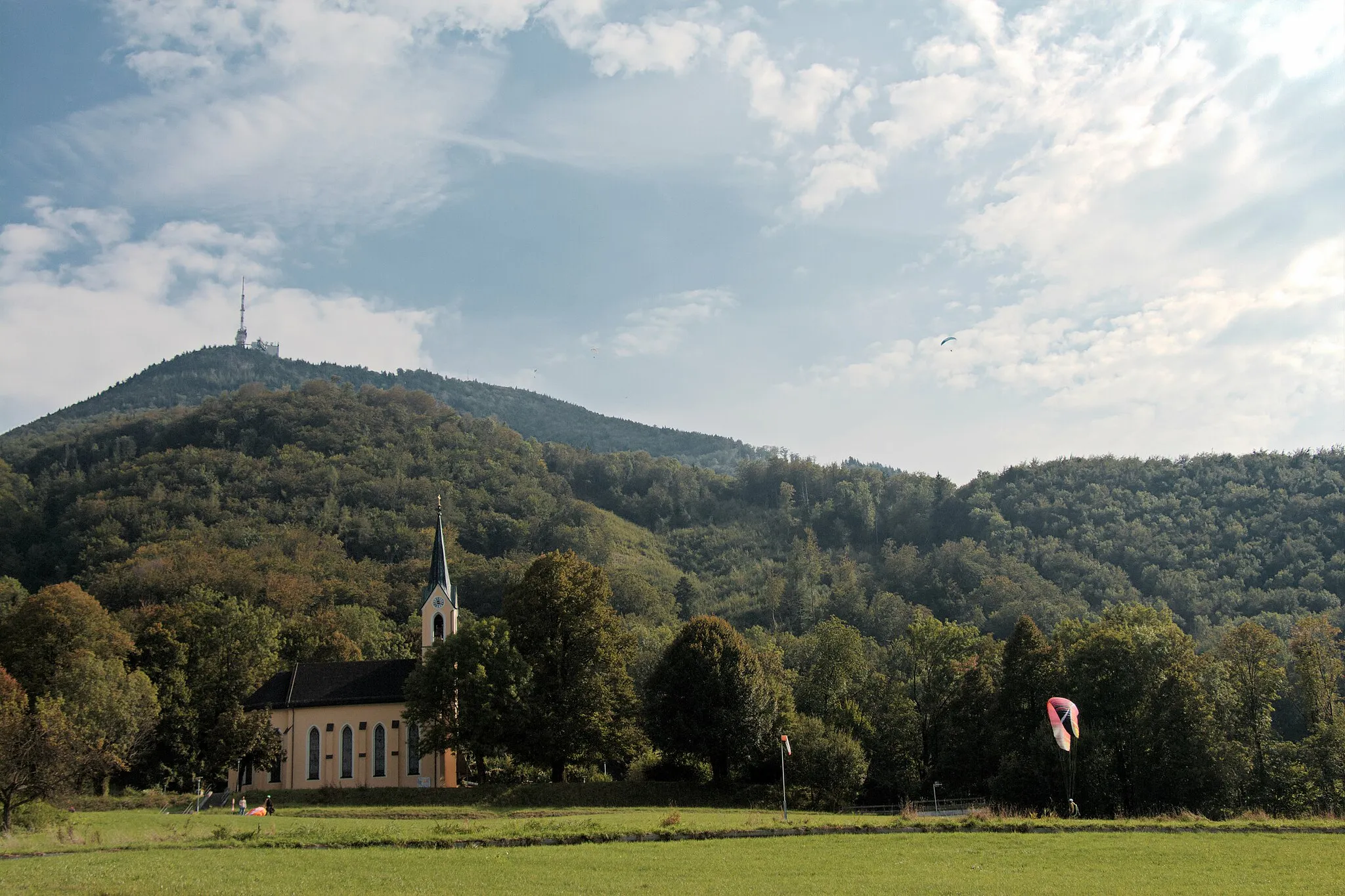 Photo showing: Filialkirche zum hl. Kreuz und zur hl. Elisabeth in Guggenthal, Gemeinde Koppl, Bezirk Salzburg-Umgebung; im Hintergrund der Gaisberg (links) und Kühberg (rechts); davor Landeplatz für Paragleiter vom Gaisberg