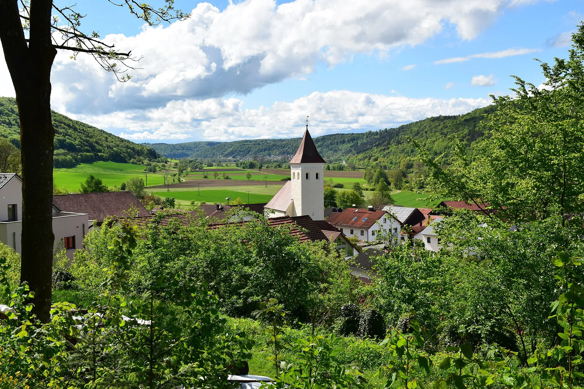 Photo showing: Teilansicht eines oberbayerischen Dorfes, Kirchturm, grünes Tal, Sonnenschein, Wolkengebilde