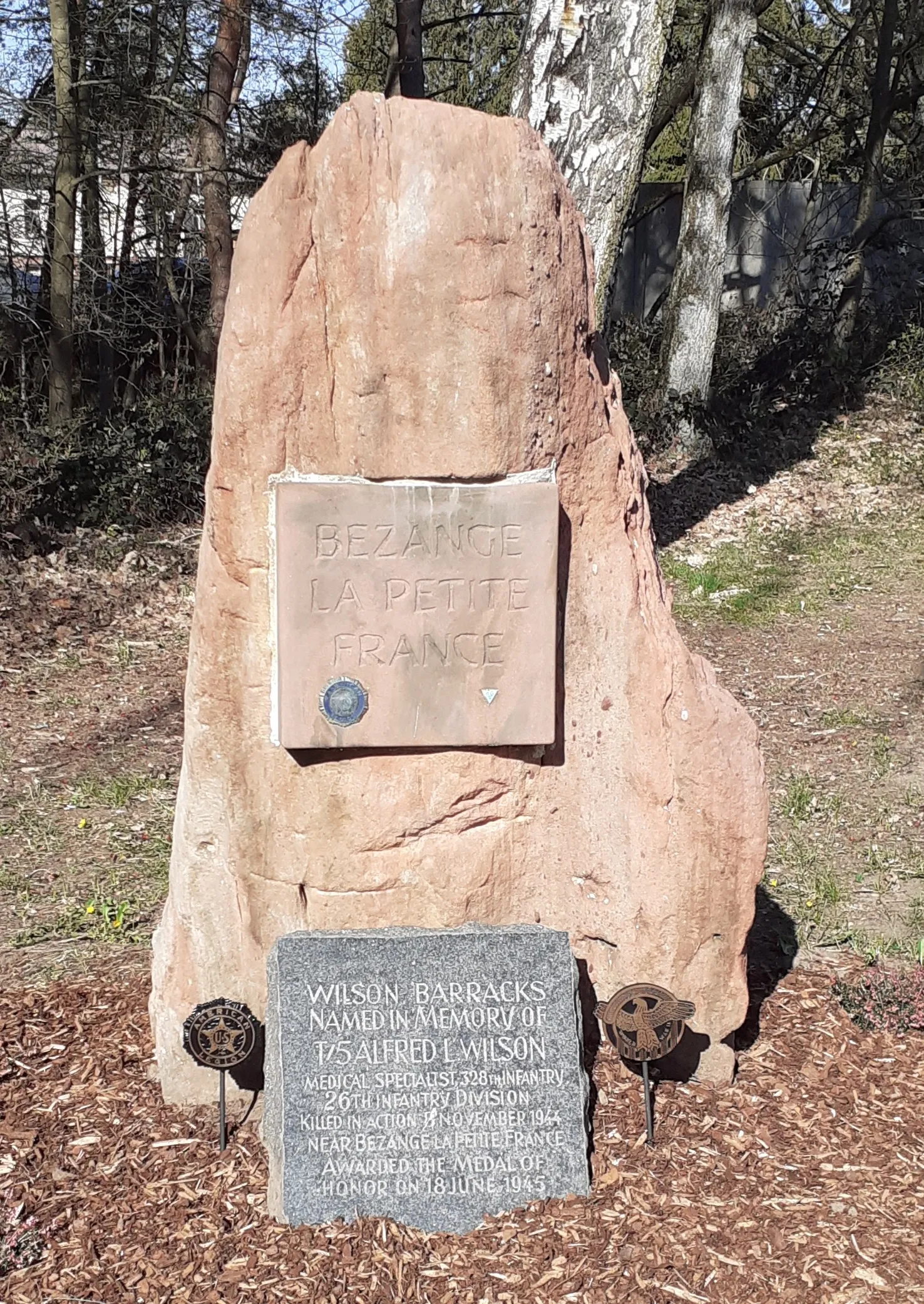 Photo showing: The Bezange la Petite Marker is a sandstone plaque located at Wilson Barracks in Landstuhl, Germany. It commemorates World War II Medal of Honor recipient Technician Fifth Grade Alfred L. Wilson, Medical Detachment, 328th Infantry, 26th Infantry Division. Wilson, for whom the barracks is named, was killed in action near Bezange la Petite, France.