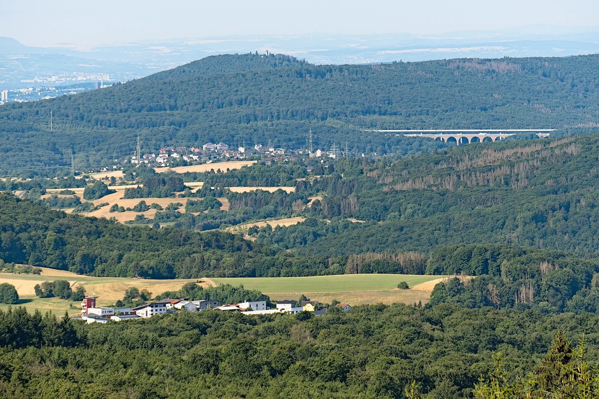 Photo showing: View from the mountain Glaskopf over the commercial park of Schlossborn on the southern part of Niederhausen as well as the Theißtal bridges for the A3 motorway and (behind) the ICE high speed railway Köln-Rhein/Main. In background, in front of Wiesbaden and the Rhein-Main area, the mountain Kellersberg with lookout can be seen.