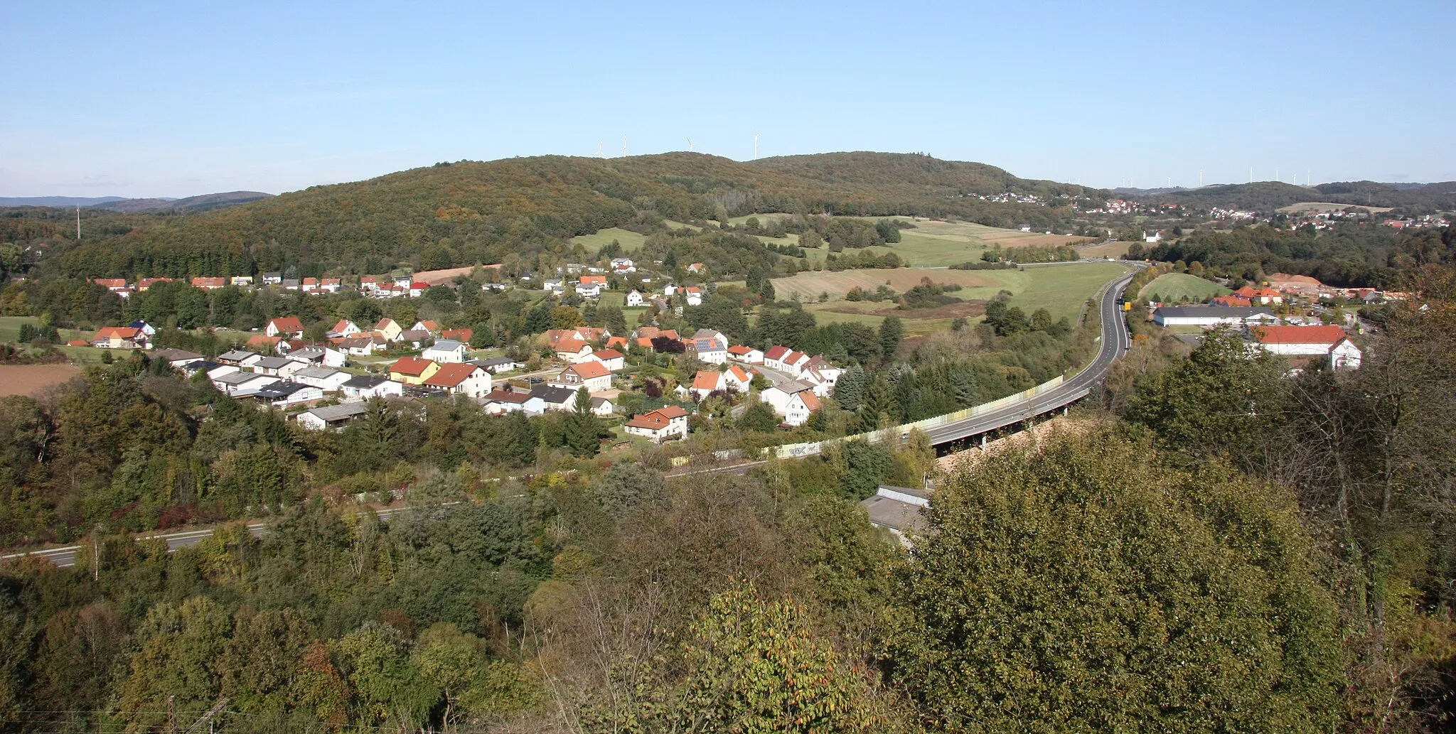 Photo showing: Eisweiler, mit „Herrenwald“ (halblinks hinten) und „Allerburg“ (mittig rechts), getrennt durch die Bundesstraße 41. Ganz links im Hintergrund: Der ehemalige TV-Umsetzer „Eisweiler“ am Namborner Bahnhof. Im Hintergrund rechts: Hirstein