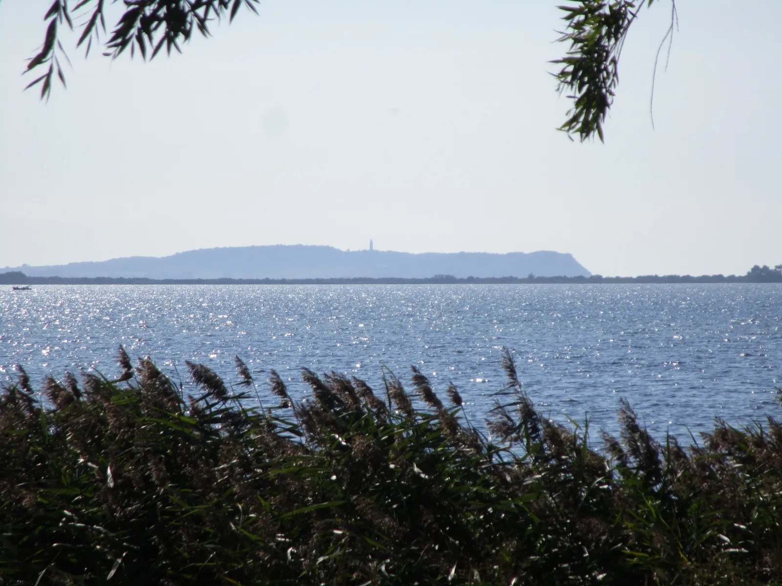 Photo showing: In der Ferne die Silhouette der Insel Hiddensee , vorne der Wieker Bodden, der Leuchtturm auf Hiddensee steht auf dem rund 70 Meter hohen Schluckwieksberg, links davon der Bakenberg als höchte Erhebung, Aufnahmestandort: nördlicher Ortsrand von Wiek (Rügen)