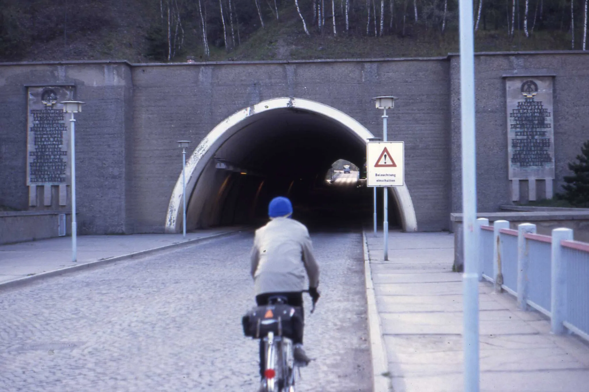 Photo showing: Close ups of the commemorative tablets either side of the tunnel entrance may be seen.....here and here
The lamp standards are very fine.  The warning sign admonishes drivers to switch on their lights....Beleuchtung einschalten.  It's dim out east in tunnels.   Is that an Ikarus bus in the light at the other end?