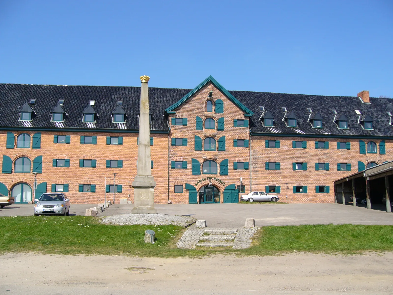 Photo showing: Das Kanalpackhaus stammt aus der Zeit des Eiderkanals, der 1784 fertiggestellt wurde. Das Lagerhaus ist 77 Meter lang. Heute enthält es Wohnung und ein Restaurant. Vor dem Packhaus steht ein Obelisk mit der Inschrift "Patriae et Populo". Auf dem Obelik befindet sich die dänische Krone.