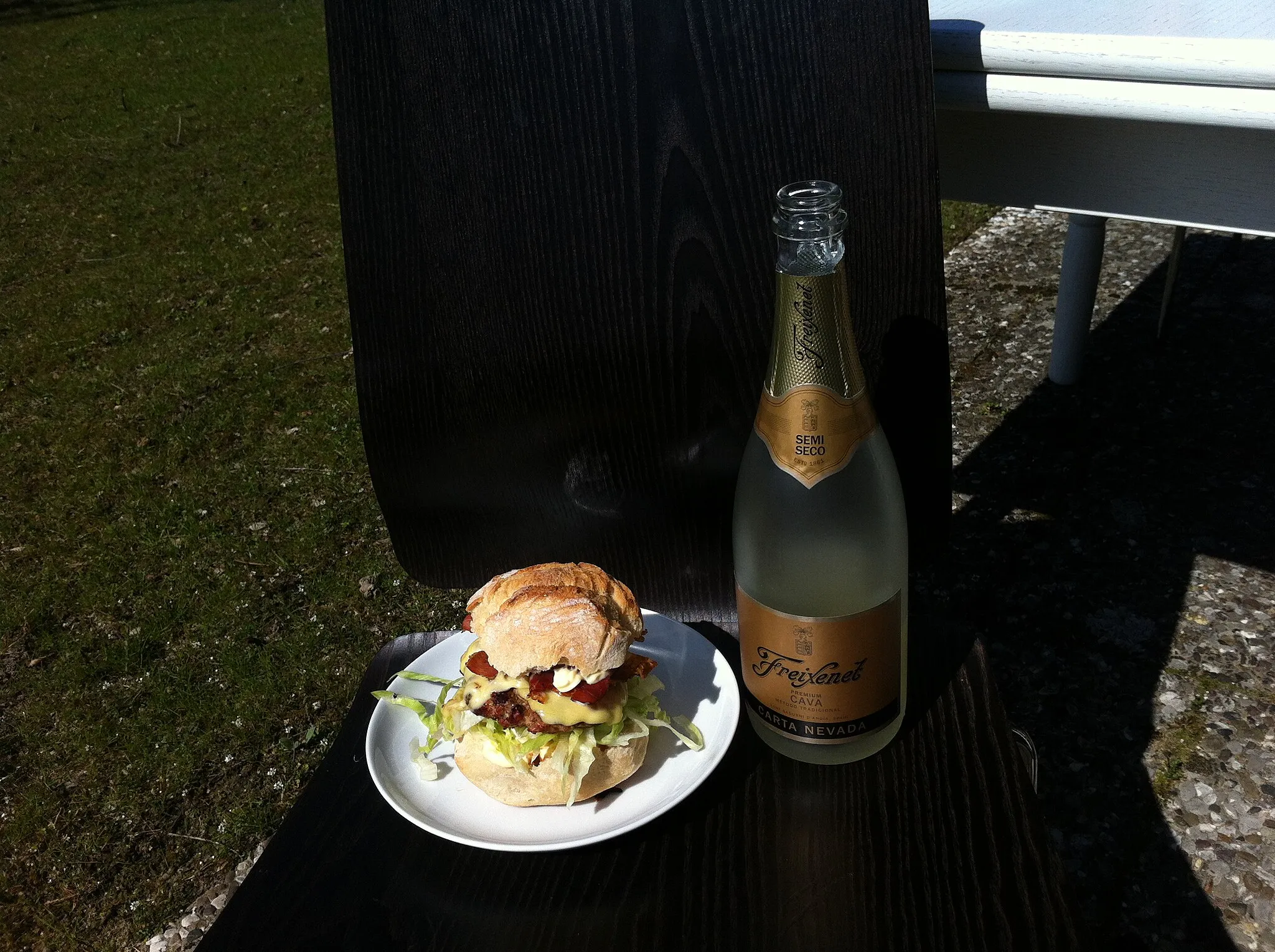 Photo showing: Grilled burger with a bottle of cava