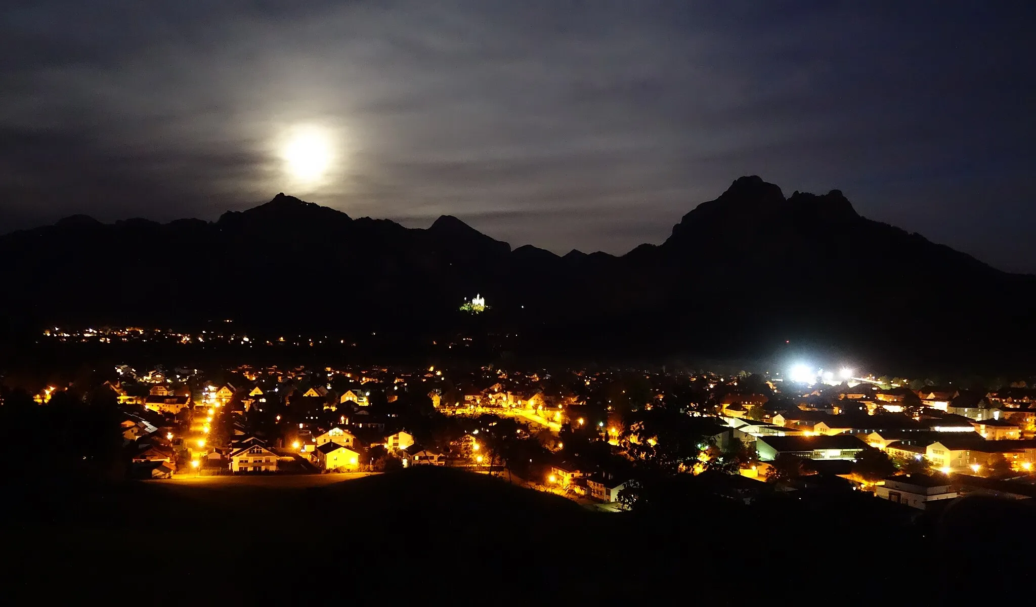 Photo showing: Füssen at night with mountains "Tegelberg" (left) and "Säuling" (right); in the middle Neuschwanstein Castle