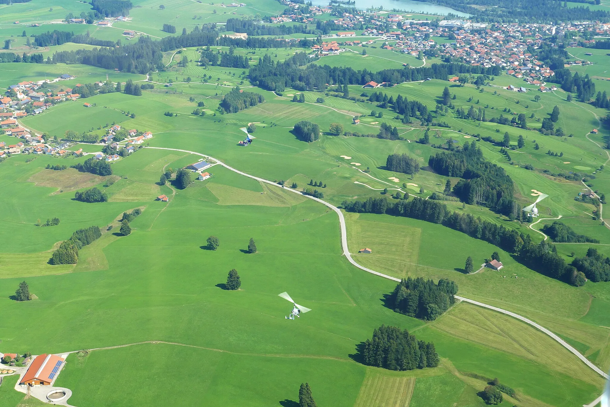 Photo showing: Golf club "Auf der Gsteig" near Lechbruck am See photographed from the gyrocopter at around 4400 feet. In the background above, the village of Lechbruck am See; also visible in the picture: Three gyroplanes in formation flight over the golf course area.