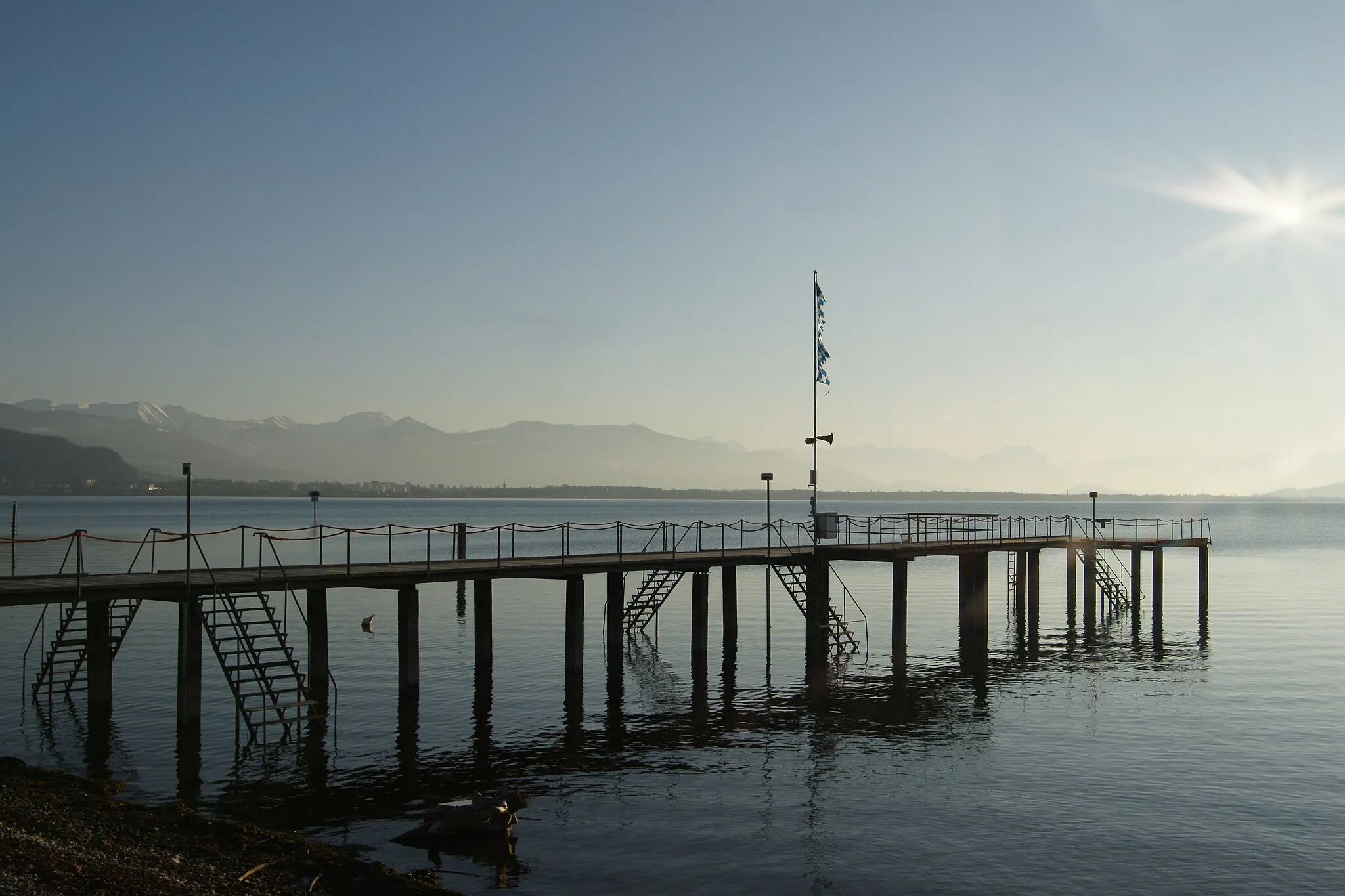 Photo showing: Steg am Strandbad von Lindau am Bodensee. Am Bildrand mit Schnee bedeckt das Bregenzerwaldgebirge mit der Dornbirner Firstkette und dem Karrenberg.