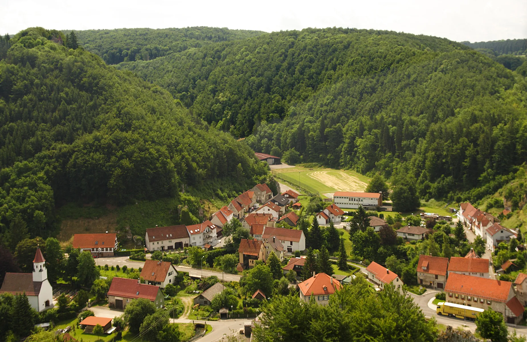 Photo showing: „Seeburg“ (Bad Urach) in the valley of the headwaters oft he Erms, heavily karstified Swabian Alb. The stream’s strong karst spring is behind the valley in ca. 1000 m. The small town rests on a travertine sediment of no less than 30 m. A former quarry wall stopped just before the “reverends house”, 12 m above the recent floor of the  Fischbach (see photo: Image:Kalktuffbarre Seeburg Ermstal Schwaebische-Alb.jpg).Several abandoned quarries are right between the towns houses, most of them refilled or hidden.
Geologists, analysing the rocks of a drilling hole, dated the travertine sediments to be of the Atlantic period (8000 B.C.). The travertine used to bloc the whole valley, impounding stream “Fischbach” to become the  lake “Bodenloser See”. “Heinrich Schickhardt”, an important builder at the court of the “Württembergers” planed and realised a water tunnel through the travertine 1617-1620 (!), this is still working and restored in 1998.