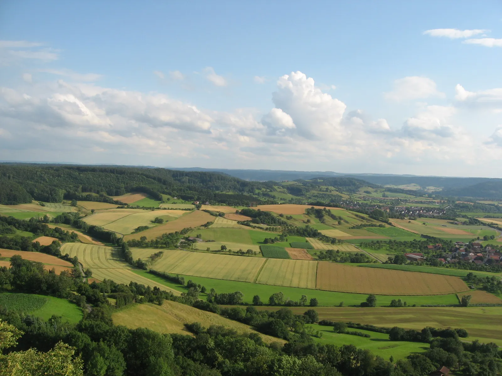 Photo showing: Blick vom Turm auf dem Einkorn bei Schwäbisch Hall-Hessental über die weite Talmulde des Remsbachs nach S. Am rechten Bildrand Michelbach an der Bilz-Rauhenbretzingen, etwas links am Waldrand auf dem ersten Hügel der Michelbacher Hagenhof, dahinter größtenteils verdeckt Michelbach selbst. Dahinter erhebt sich unter der hohen Cumulus-Wolke noch vor dem dunstigen Horizont das kleine Bergmassiv aus Buchhorn und Adelberg.