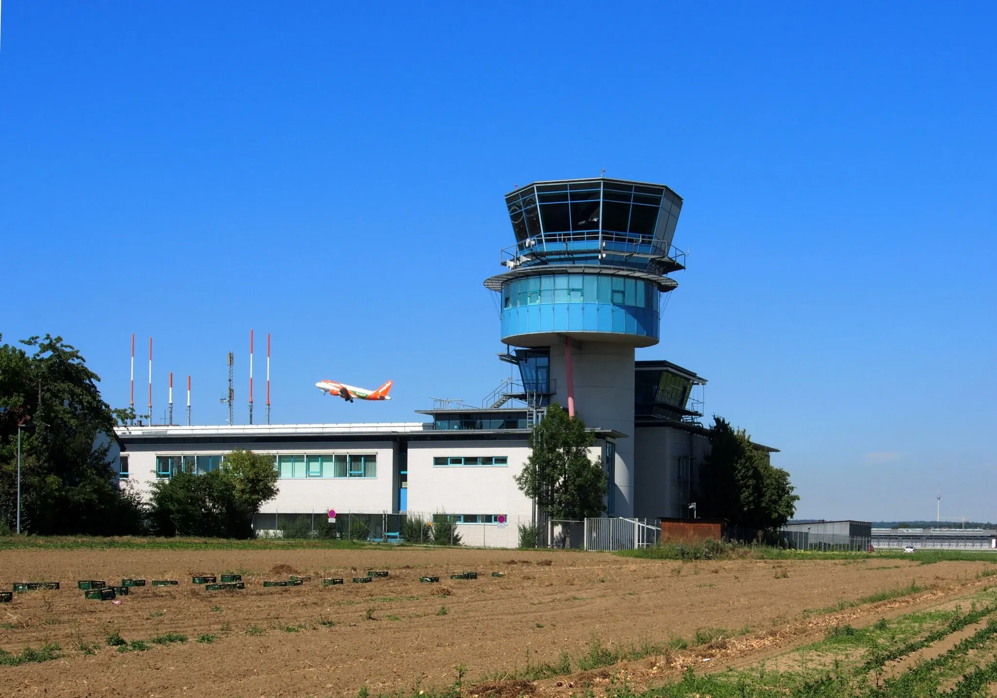Photo showing: Tower des Flughafens Stuttgart in Bernhausen, gesehen vom Nord-Ost-Ring, mit startendem Flugzeug. Im Hintergrund der Fernsehturm.