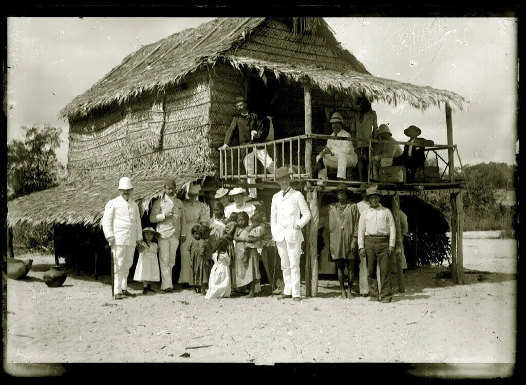 Photo showing: Groepsfoto van het reisgezelschap van de gouverneur Titus van Asch van Wijck met enkele indianen voor een woning in het kamp van Surinaamse indianen aan de Donders Kreek bij de Wayombo Rivier, 6 augustus 1895. Op de foto staan: Dhr. en mevr. van Asch van Wijck, Arthur en Freda Kool, Dolly van Lelyveld-van Emden, P. ten Bruggen Cate, Dhr. von Weiler, Dr. H.D. Benjamins en Mr. G.H. Barnet Lijon.