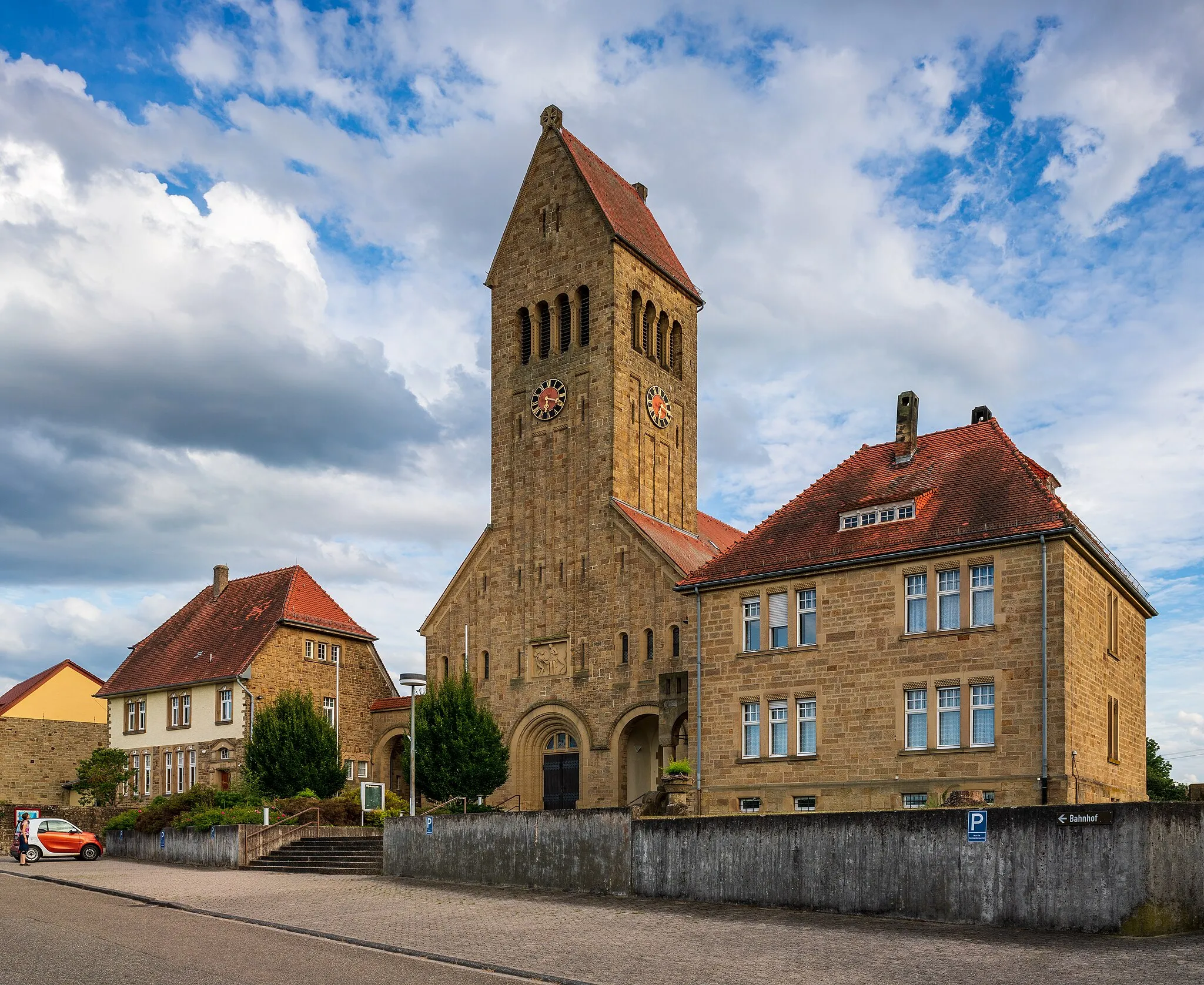 Photo showing: Oberderdingen, Germany, district Flehingen: the Saint Martin church, built in 1911 in Romanesque revival style together with the buildings at the left and right (rectory and kindergarden). View from northwest with evening sun. Hint: I have included by way of exception the person and the car intentionally because the church had such an surreal or computer-generated effect that I wanted the person and the car as signs of reality ;–).