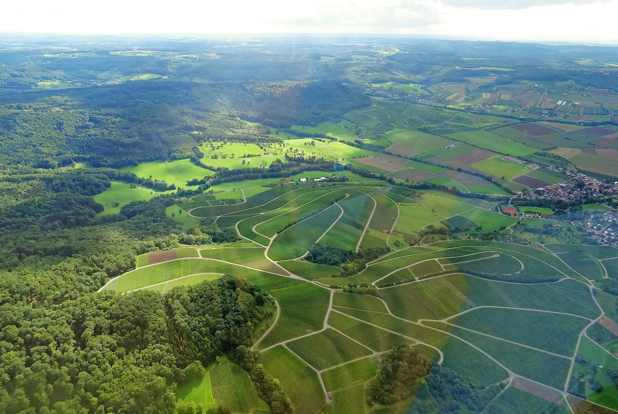 Photo showing: Aerial view of the vineyard of Michelbach Am Wald, district of Öhringen. Part of Michelbach can be seen in the centre of the picture on the right. The educational wine trail begins at the sports facilities there. In the photo there are slight reflections from the gyroplane cockpit.
