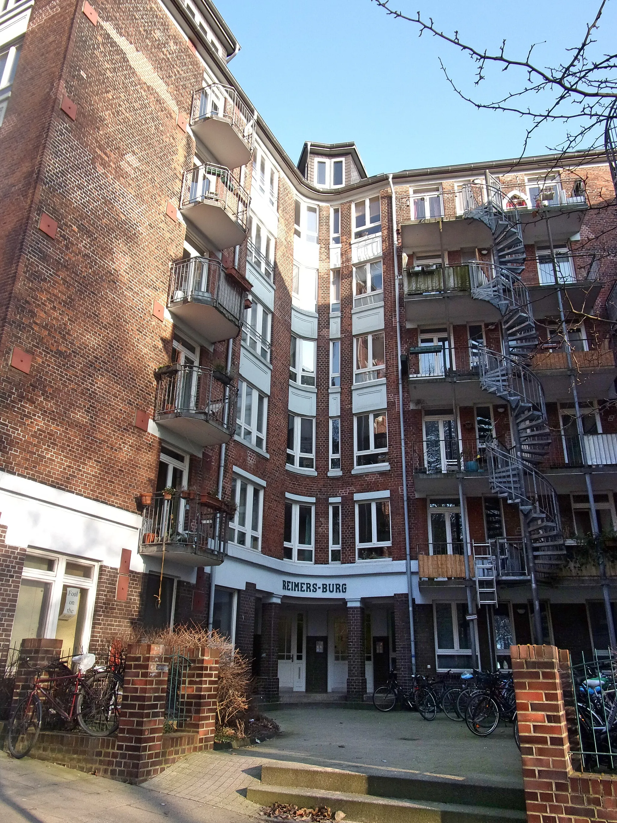 Photo showing: Die Reimers-Burg ist ein typisches Beispiel für eine Hamburger Burg. Solche Wohnburgen sind das Gegenteil von den früheren Gängevierteln in Hamburg, wo man in Hinterhöfen mit schlechten Luft- und Lichtverhältnissen wohnte und nur die Vorderhäuser genügend Tageslicht bekamen. Man setzte die Häuser ein Stück zurück um einen Platz vor dem / die Häuser zu schaffen, meist Dreiflügelbauten mit Fenstern nach vorne.Die Reimers-Burg befindet sich am Kuhberg in der südlichen Neustadt.