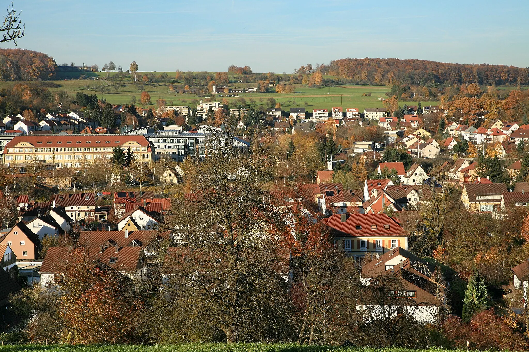 Photo showing: View of Faurndau, a district of Göppingen. In the middle of the picture on the left is the building of the former Salamander shoe factory (listed) erected in 1912 and behind it the computer center of Telekom. In the background the area of the Wangener Linde.