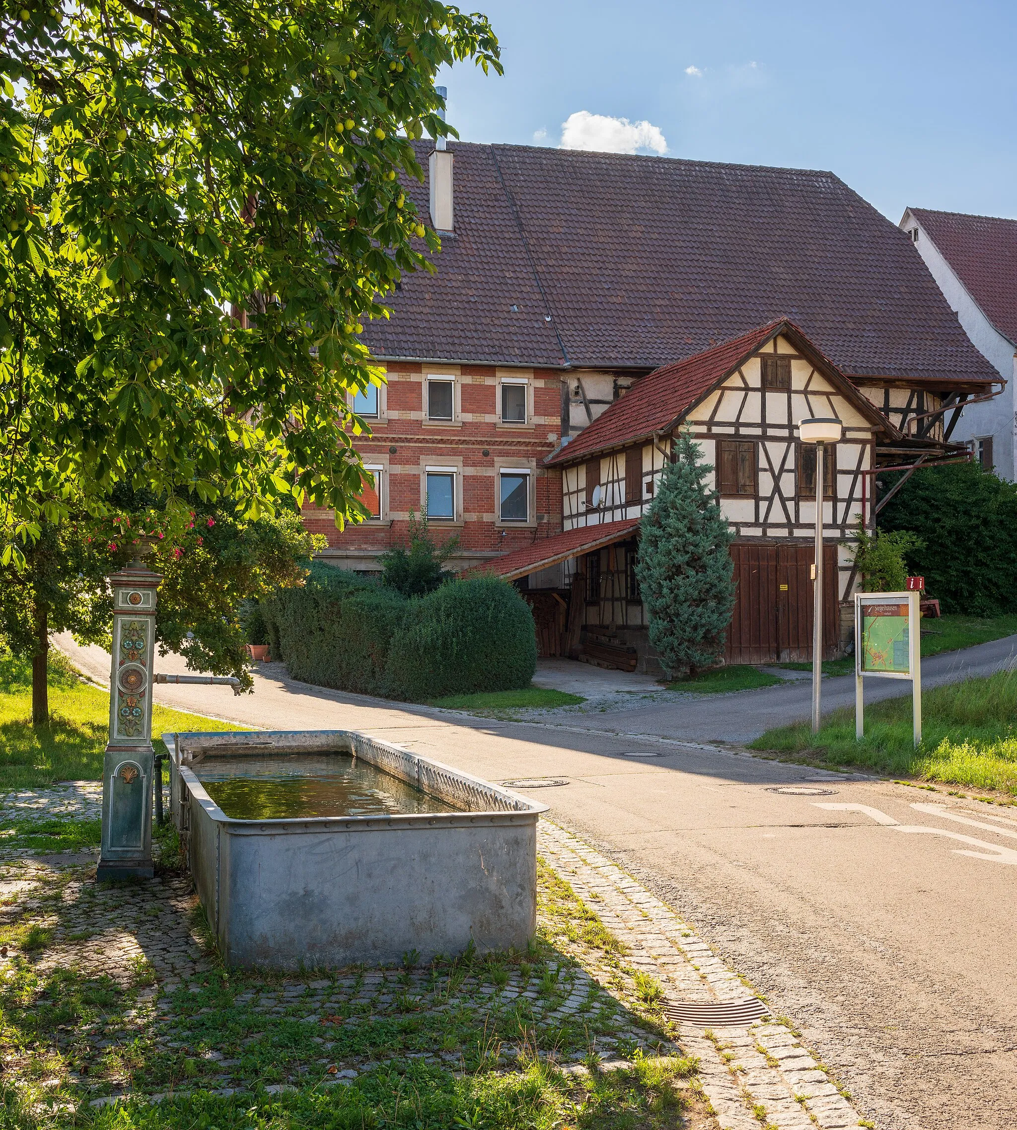 Photo showing: Siegelhausen (Ortsteil von Marbach am Neckar, Landkreis Ludwigsburg): das Zentrum des Weilers mit dem gusseisernen, bemalten Aufbaus des Dorfbrunnens aus dem 19. Jahrhundert und dem historischen Bauernhof Siegelhausen 1 im Hintergrund.