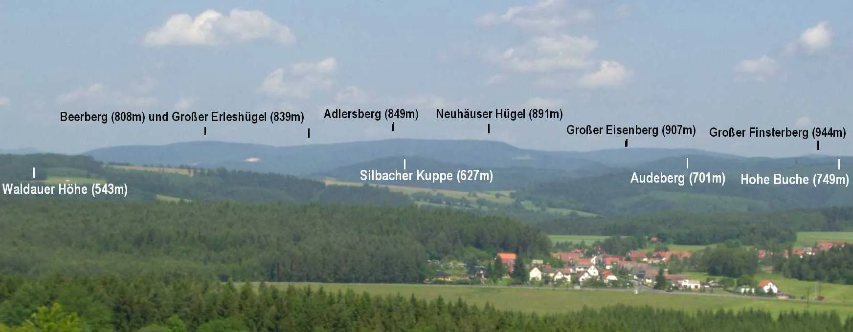 Photo showing: Blick vom Ahornsberg (15km südlich) auf den nach Süden dominanten Adlersberg (849m) mit seinen 808-891m hohen Nebengipfeln und den Großen Eisenberg (907m); rechts, halb verdeckt, der Große Finsterberg (944m); im Vordergrund der Ort Schwarzbach