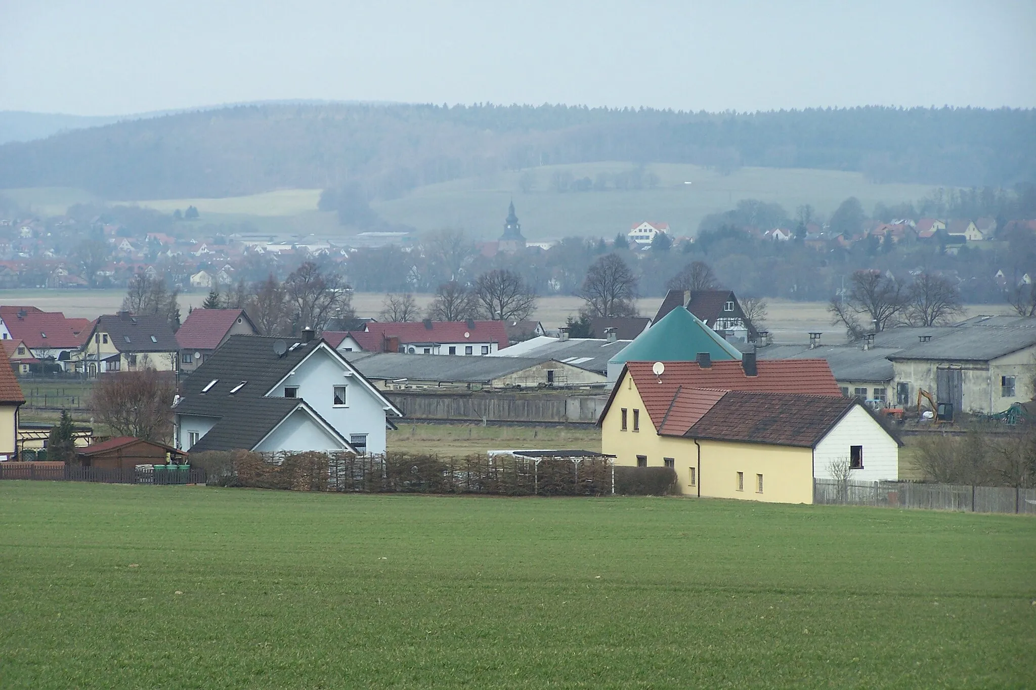 Photo showing: Vordere Häuserzeile ist das Neubaugebiet am Westrand von Hermannsroda, in Bildmitte, hinter den Lagerhallen liegt Kaiseroda, dahinter, bereits jenseits der Werra, Tiefenort (mit Kirche).