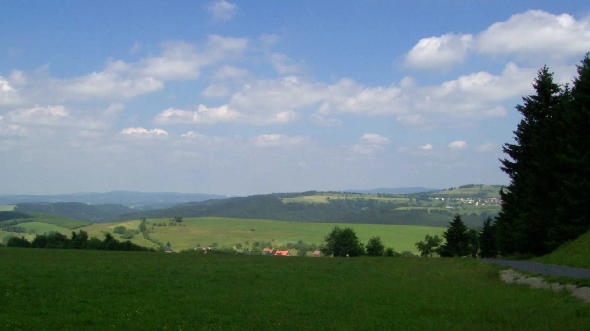 Photo showing: Blick vom Eckartsberg auf Schnett und den Simmersberg (781m, rechts) mit seinem Nebengipfel Kohlberg (718m, Mitte). Dazwischen ist im Hintergrund der Adlersberg (849m) mit dem Neuhäuser Hügel (891m) erkennbar. Links des Kohlberges folgen im Hintergrund das Gewerbegebiet Suhl-Friedberg und der Kleine Thüringer Wald mit Schleusinger Berg (671m) und Schneeberg (692m). Mittig im Vordergrund der Ort Waffenrod-Hinterrod.