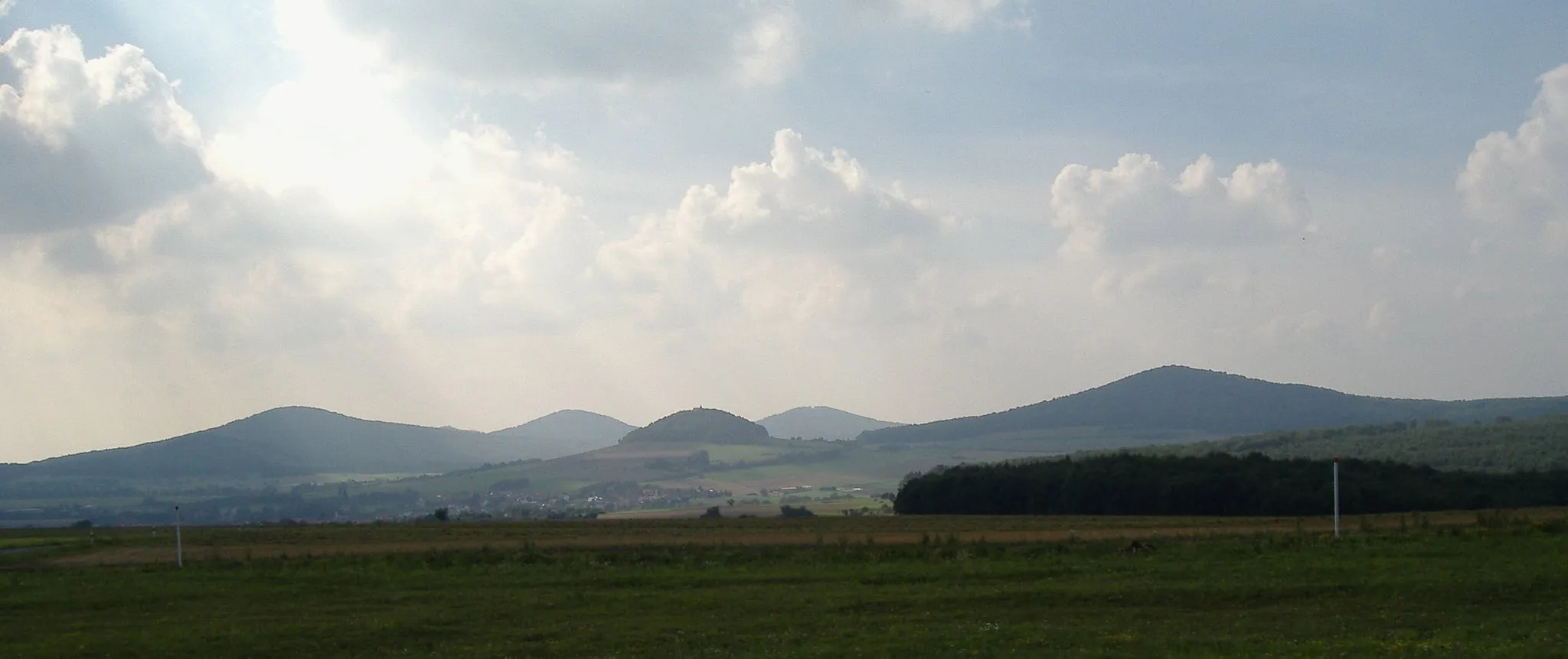 Photo showing: Das Hessische Kegelspiel von nah dem Haus der Grenze, Gedenkstätte Point Alpha an der Landesstraße Rasdorf–Geisa mit (vlnr):
Stallberg (553 m; 6 km)
Appelsberg (532 m; 7 km)
Geholfersberg (456 m; 3 km)
Rückersberg (525 m; 8 km)
Kleinberg (522 m; 4 km) Kaum zu erkennen sind der Morsberg (466 m; 5 km) vor der linken unteren Flanke des Stallbergs und die Spitze des Wisselsbergs (518 m; 9 km) hinter der rechten Flanke desselben.

Vgl. Udeuschle